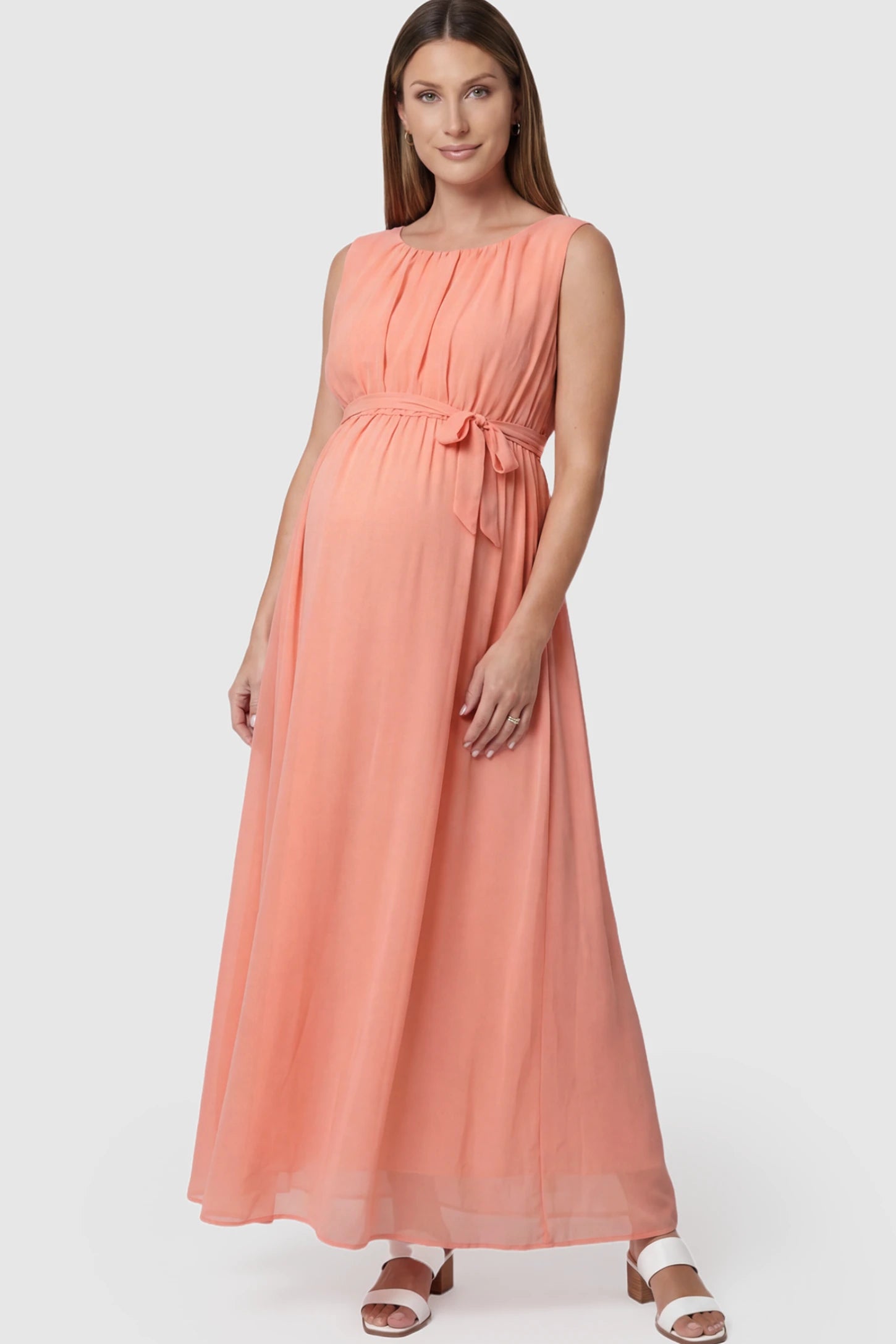 Empire Waist Tie-Front Sleeveless Maternity Maxi Dress Empire Waist Tie-Front Sleeveless Maternity Maxi Dress in Pink featuring a tie front and empire waist on a pregnant model posing front.