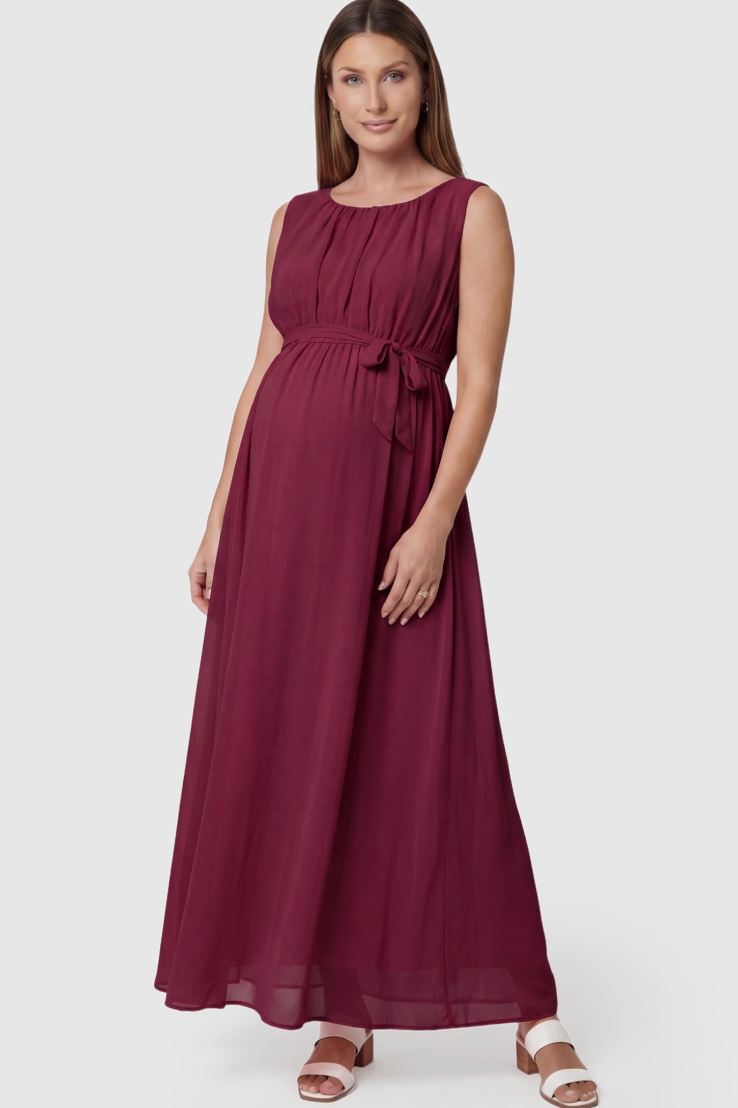 Empire Waist Tie-Front Sleeveless Maternity Maxi Dress Empire Waist Tie-Front Sleeveless Maternity Maxi Dress in Wine Red featuring a tie front and empire waist on a pregnant model posing front.