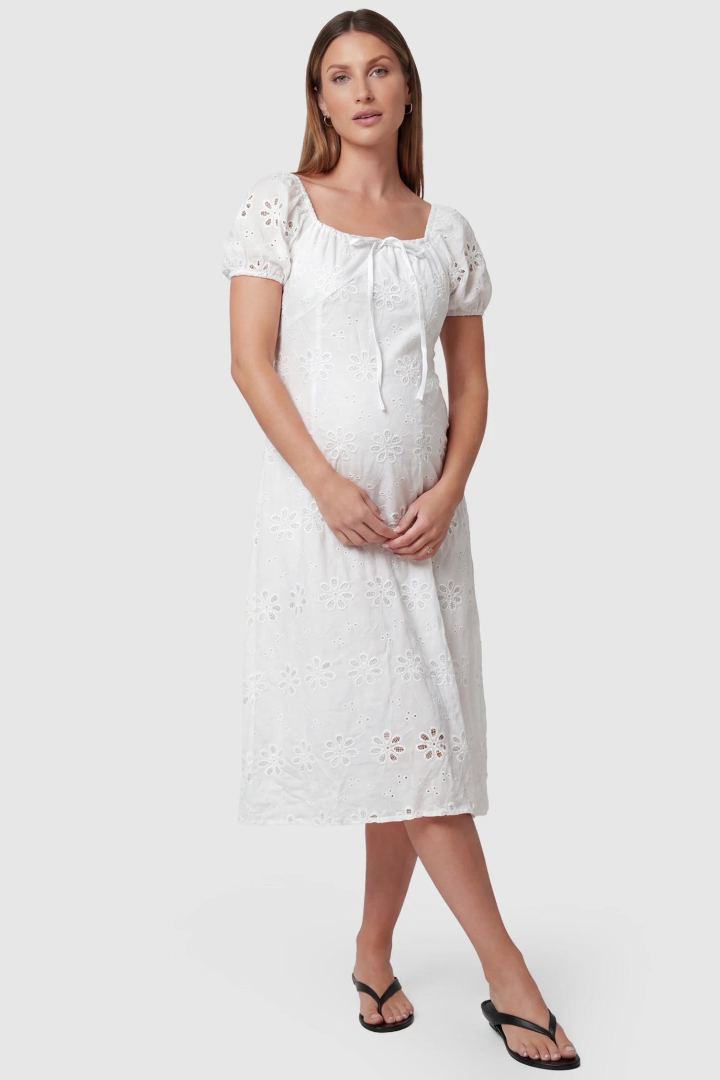 Eyelet Embroidered Short Sleeve Maternity Midi Dress Eyelet Embroidered Short Sleeve Maternity Midi Dress in white featuring a square neckline and drawstring waist on a pregnant model, front view.