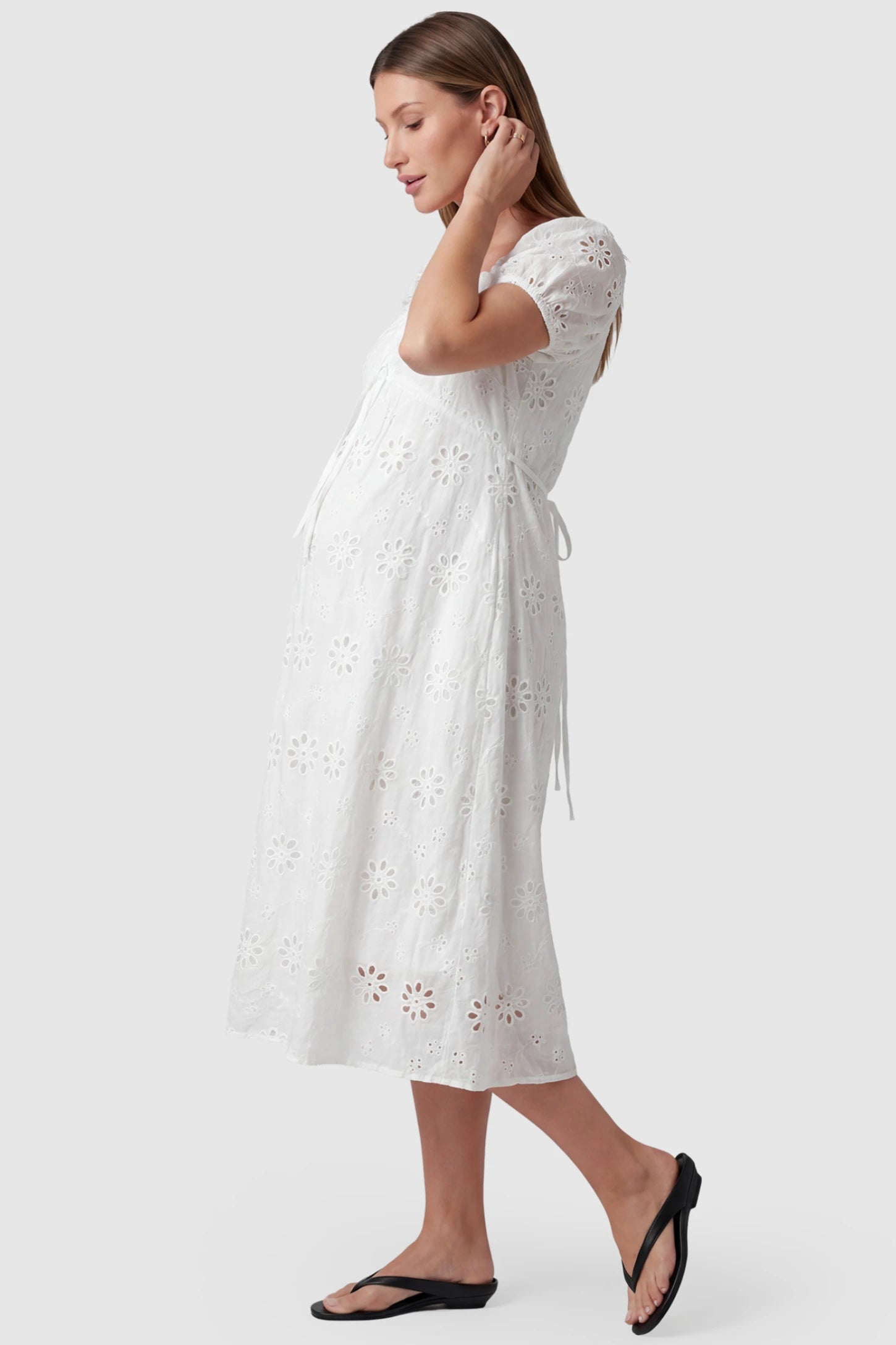 Eyelet Embroidered Short Sleeve Maternity Midi Dress Eyelet Embroidered Short Sleeve Maternity Midi Dress in white featuring a tie-back drawstring waist on a pregnant model, side view.