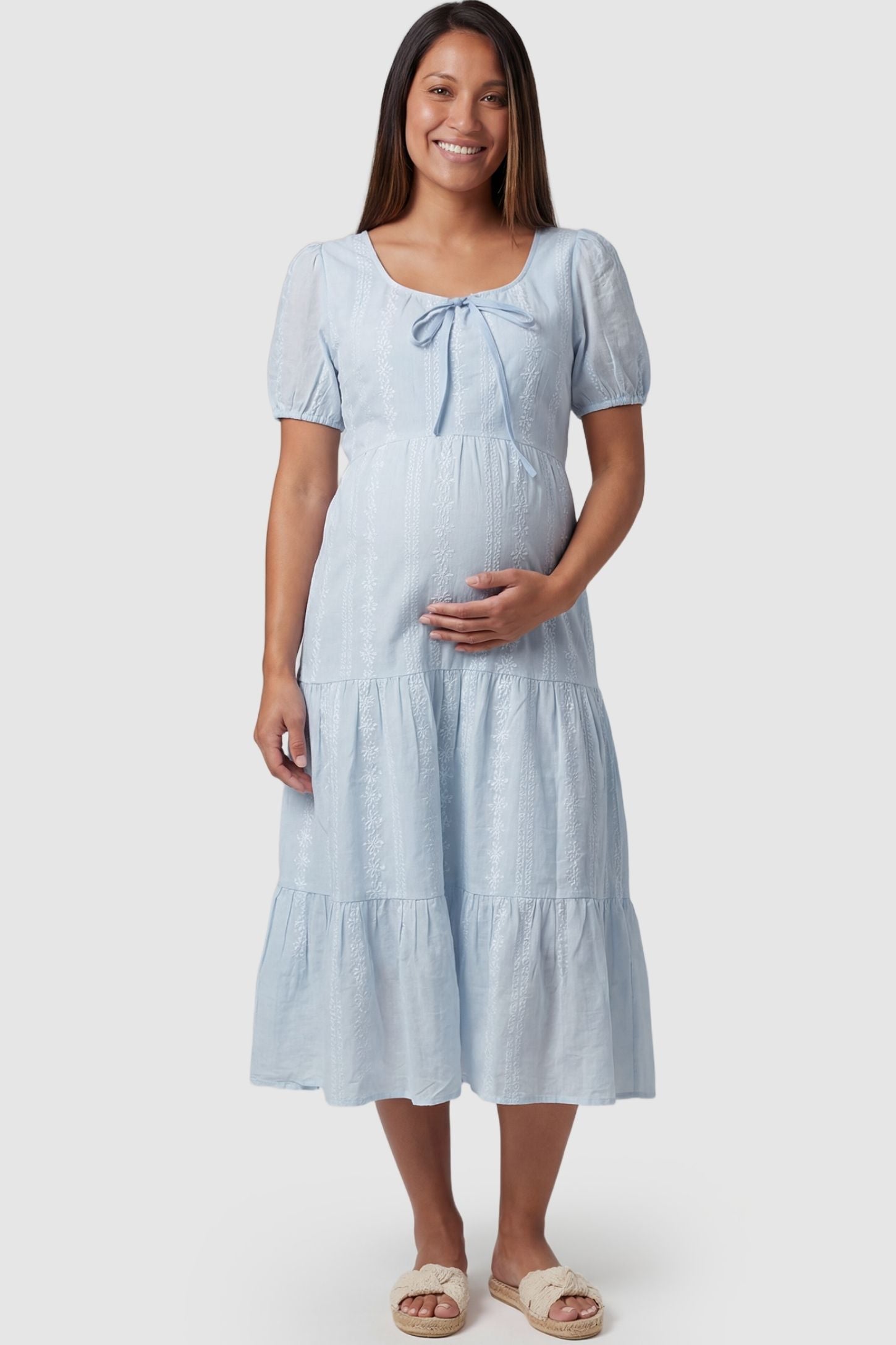 Eyelet Scoop Neck Tiered Maternity Dress in Blue featuring a front tie detail on a pregnant model, front view.