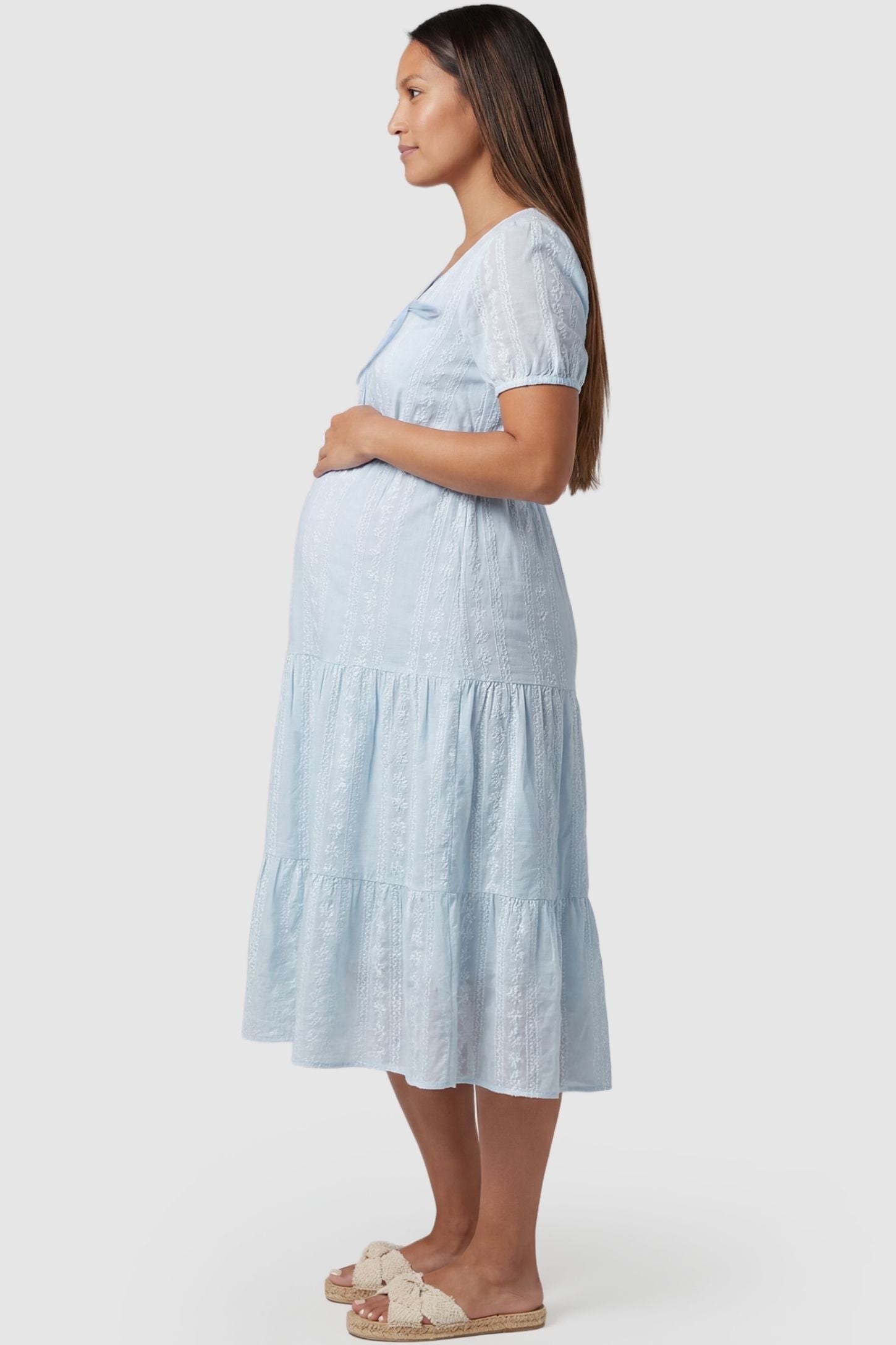 Eyelet Scoop Neck Tiered Maternity Dress Eyelet Scoop Neck Tiered Maternity Dress in Blue featuring a tiered flounce skirt on a pregnant model, side view.