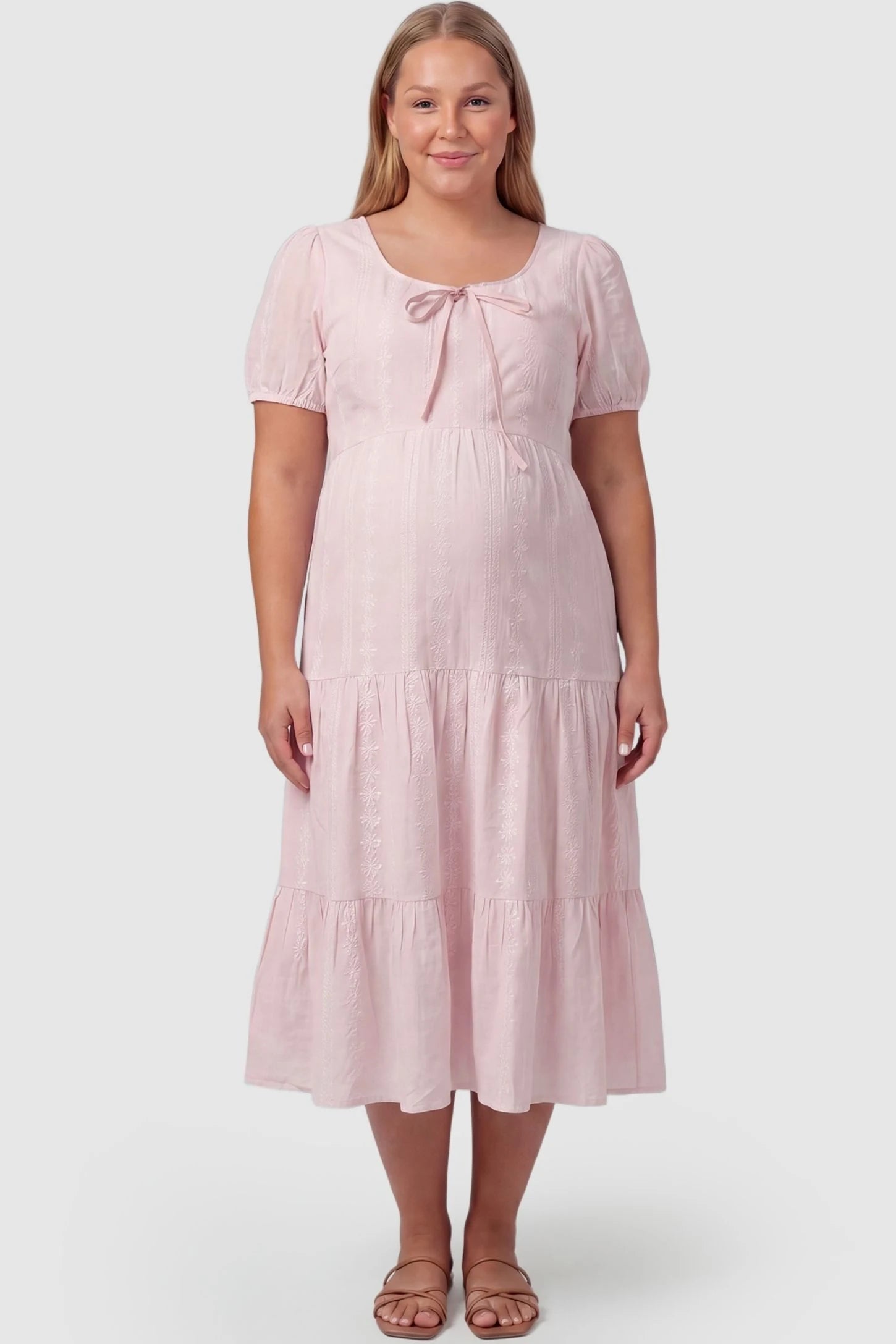 Eyelet Scoop Neck Tiered Maternity Dress Eyelet Scoop Neck Tiered Maternity Dress in Pink featuring a front tie detail on a plus size pregnant model, front view.