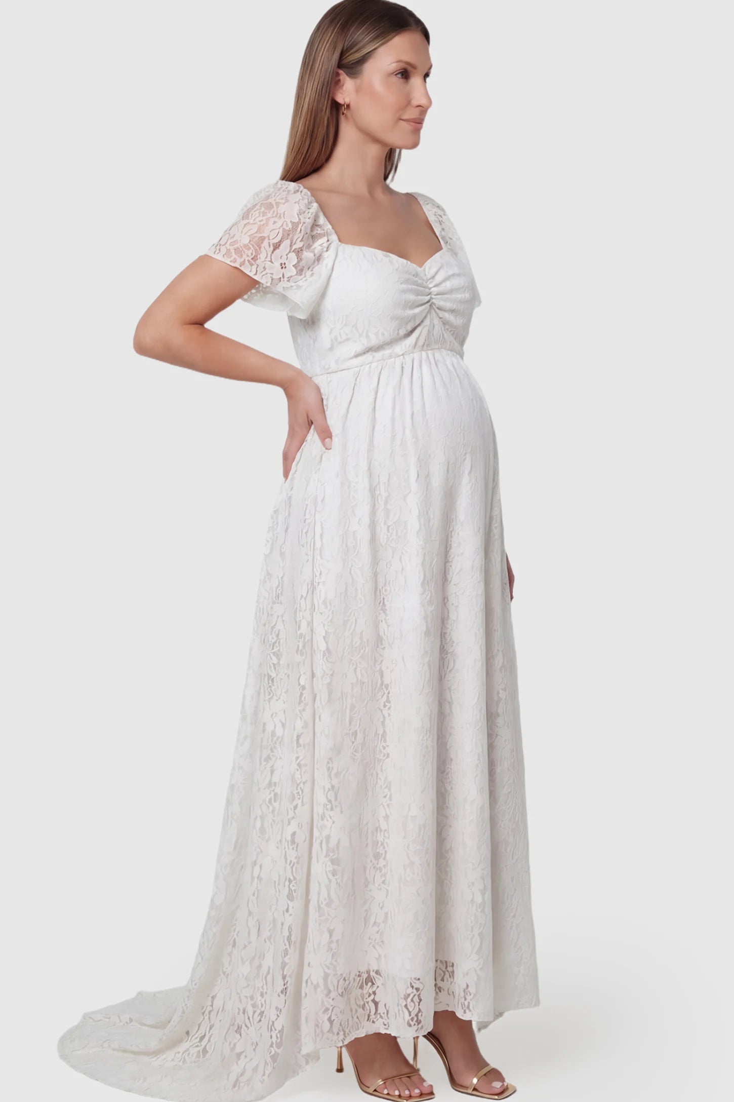 Floral Lace Flutter Sleeve Maternity Maxi Dress Floral Lace Flutter Sleeve Maternity Maxi Dress in White featuring sweetheart neckline on a pregnant model showing side.