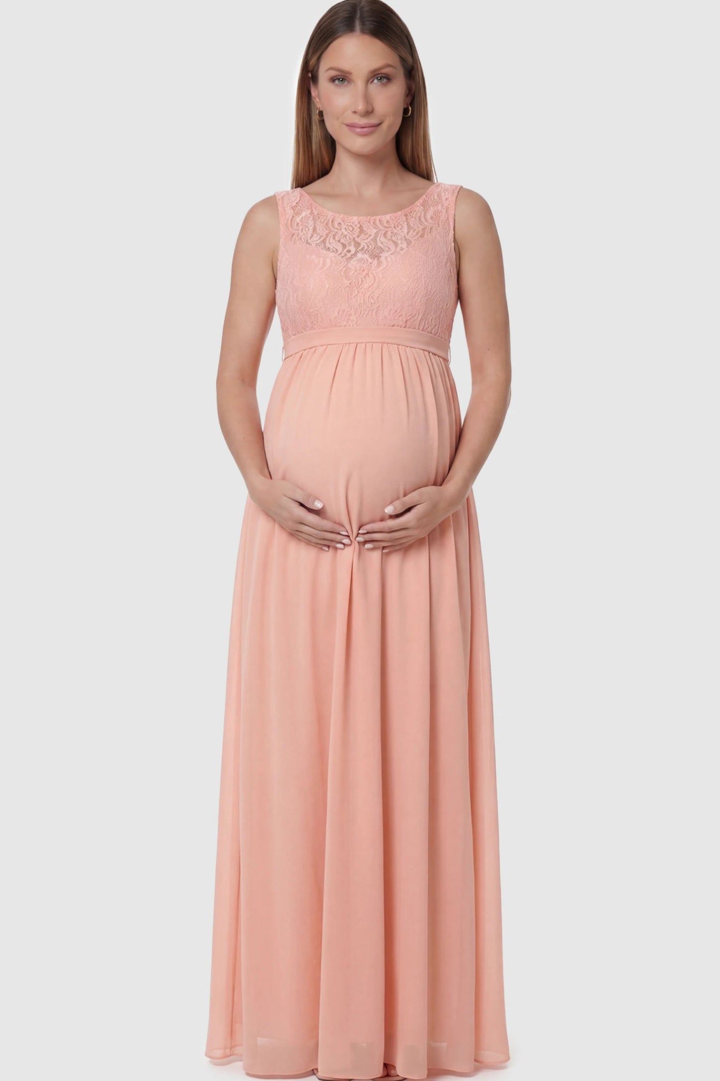 Floral Lace Sleeveless Maternity Maxi Dress Floral Lace Sleeveless Maternity Maxi Dress in Pink featuring a flowing skirt on a pregnant model posing front.