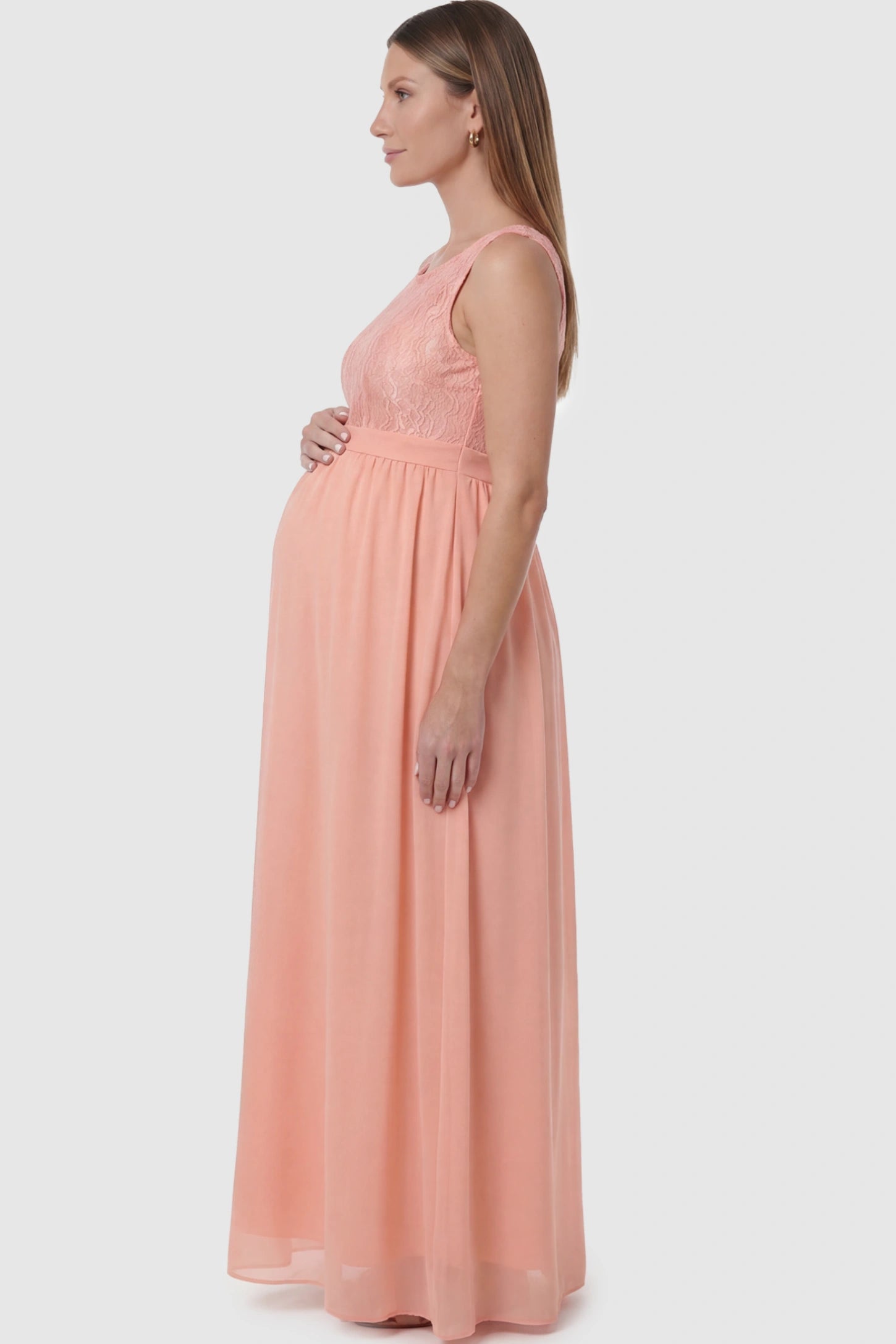 Floral Lace Sleeveless Maternity Maxi Dress Floral Lace Sleeveless Maternity Maxi Dress in Pink featuring a flowing skirt on a pregnant model showing side.