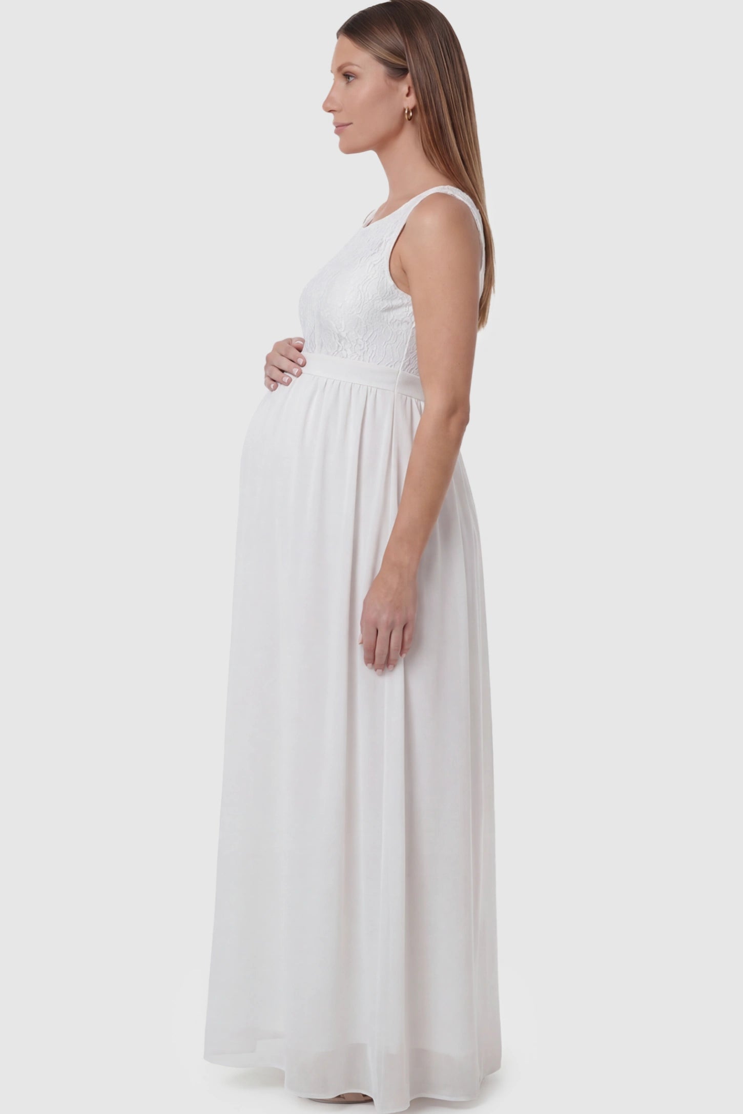 Floral Lace Sleeveless Maternity Maxi Dress Floral Lace Sleeveless Maternity Maxi Dress in White featuring a flowing skirt on a pregnant model showing side.