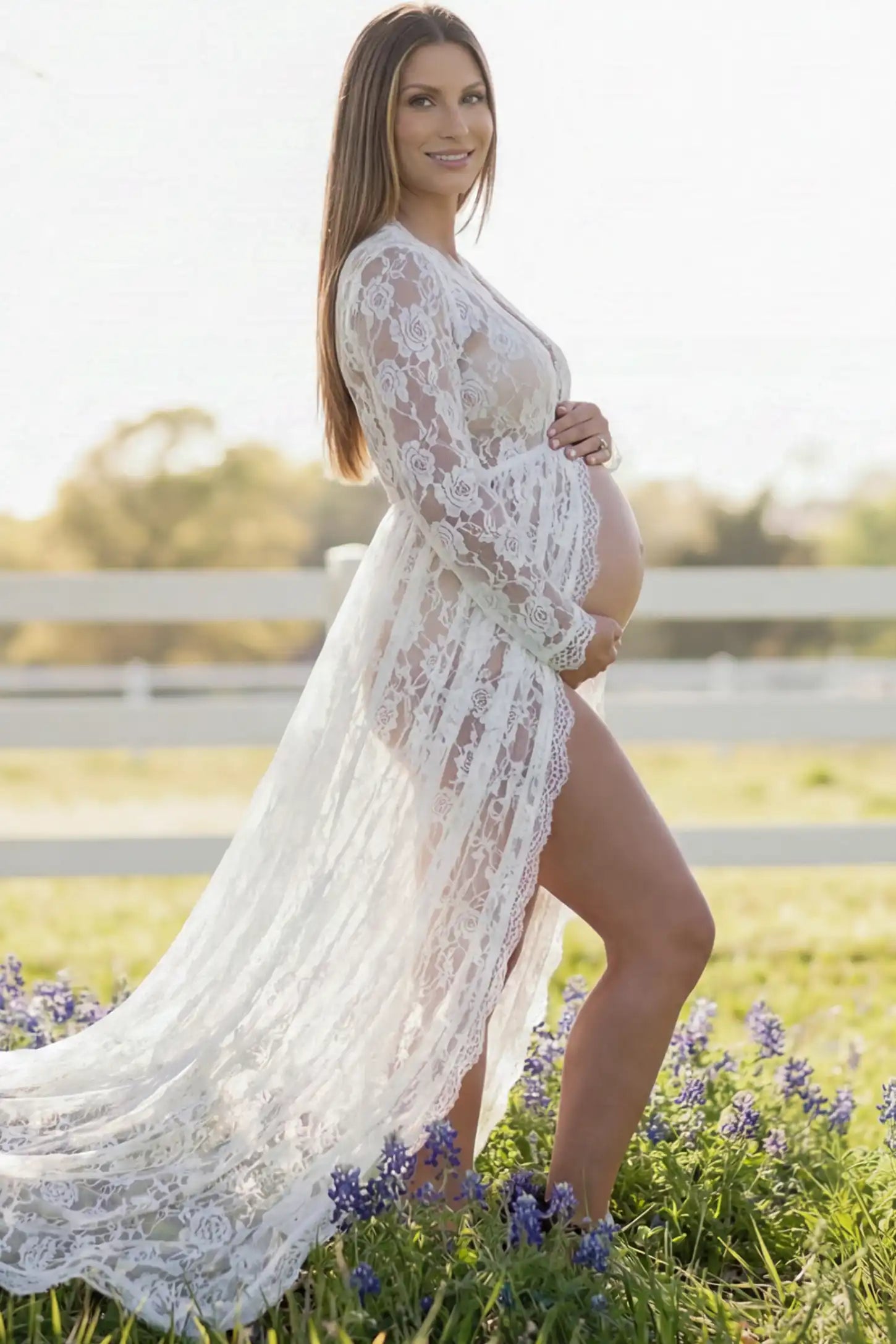 Floral Lace V-Neck Long Sleeve Maternity Photoshoot Gown Floral Lace V-Neck Long Sleeve Maternity Photoshoot Gown in White featuring long sleeves and high front slit on a pregnant model showing side.