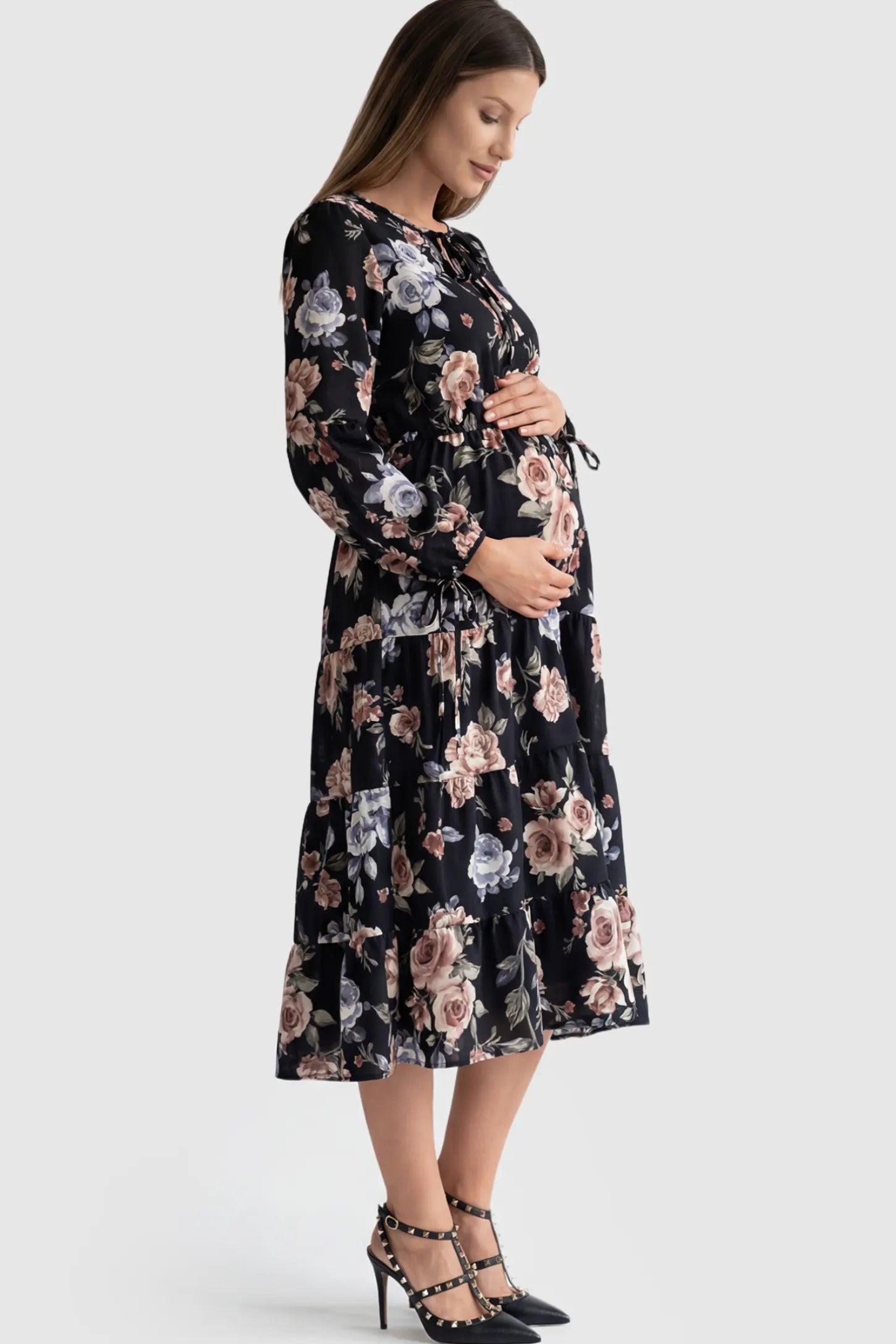 Floral Print Tiered Maternity Midi Dress Floral Print Tiered Midi Maternity Dress in dark floral featuring adjustable tie-cuff sleeves on a pregnant model showing side.