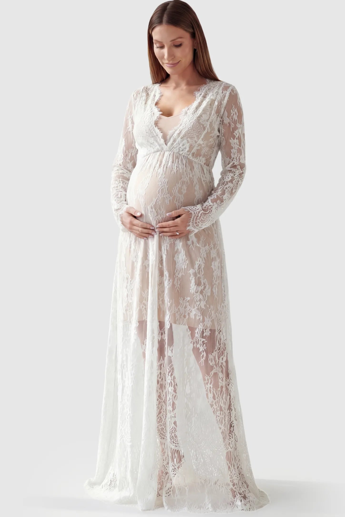 Floral Sheer Lace Long Sleeve Maternity Photoshoot Gown Floral Sheer Lace Maternity Gown in White featuring scalloped v-neck and long sleeves on a pregnant model showing front.