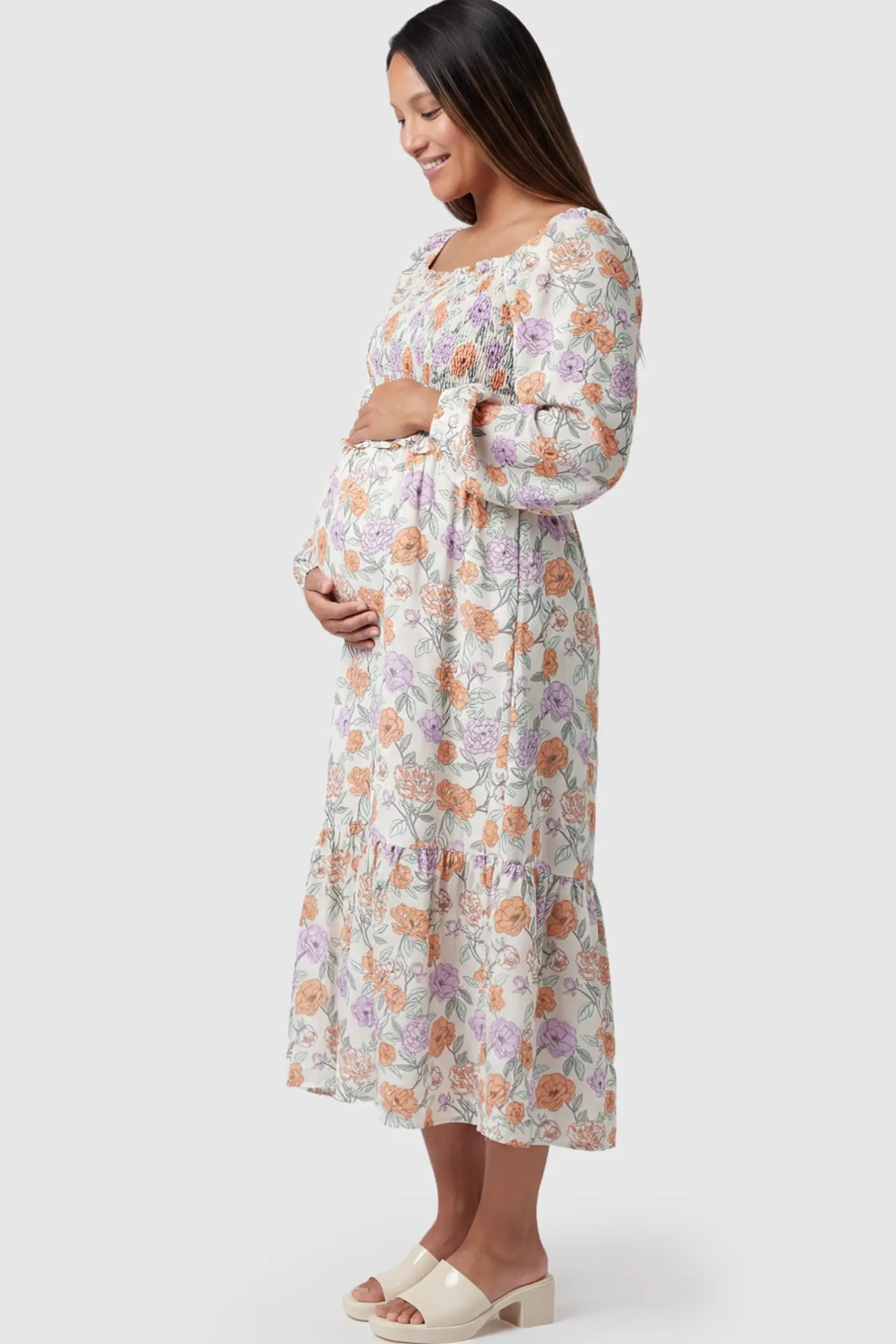 Floral Smocked Bodice Tiered Maternity Midi Dress Floral Smocked Bodice Tiered Midi Dress in floral print featuring a smocked square neckline on a pregnant model showing side.