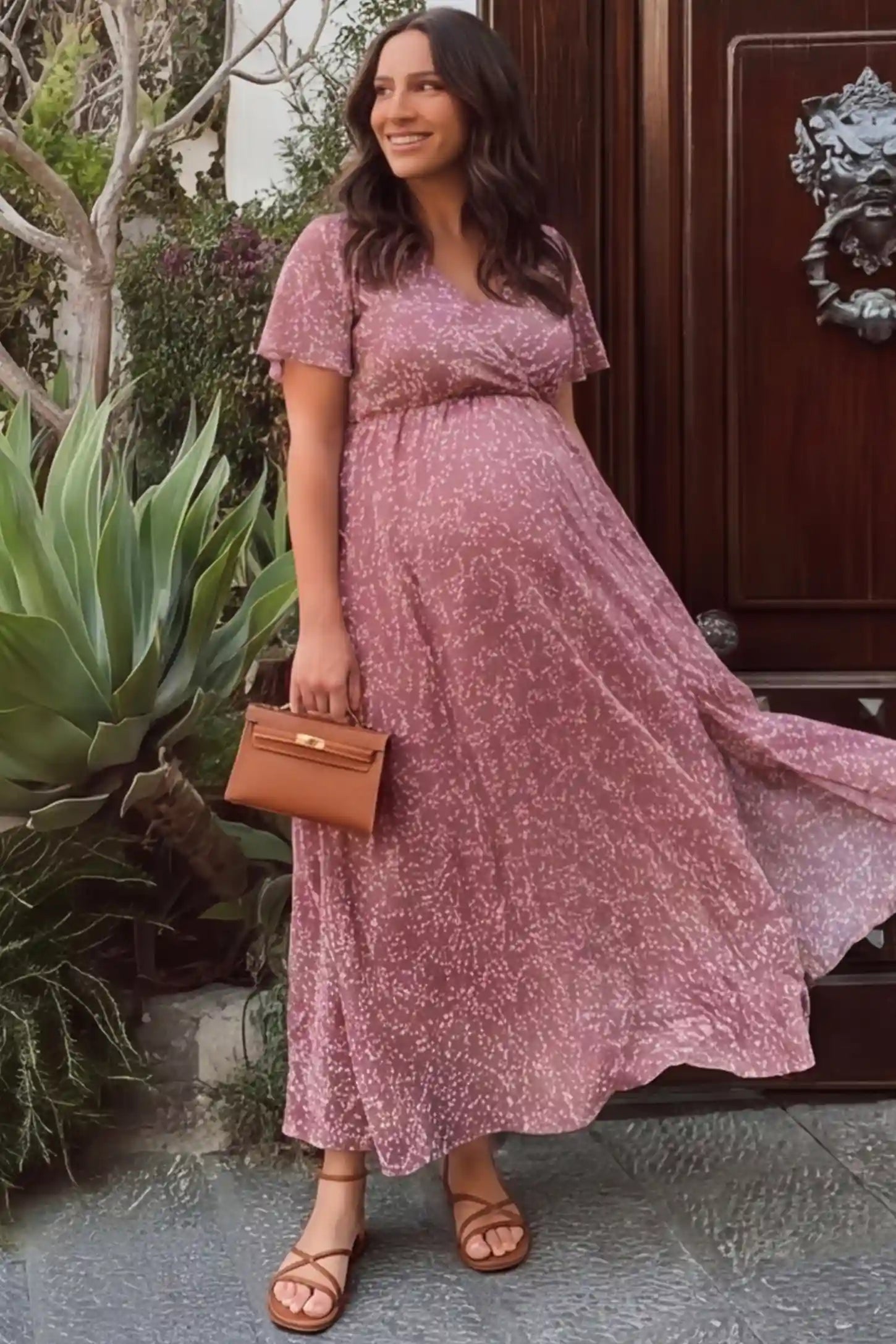Floral V-Neck Side-Slit Maternity Maxi Dress Floral V-Neck Side-Slit Maternity Maxi Dress in pink featuring a delicate white floral print and a wrap-style bodice, shown on a pregnant woman outdoors by a garden entryway, front view.