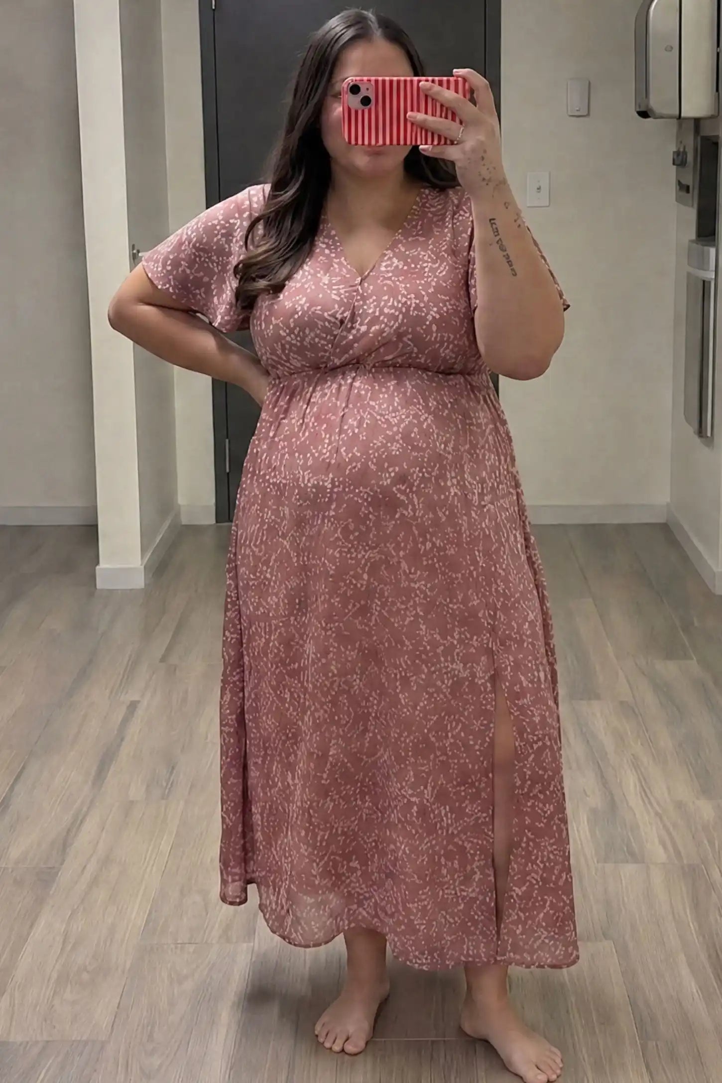 Floral V-Neck Side-Slit Maternity Maxi Dress Floral V-Neck Side-Slit Maternity Maxi Dress in pink featuring short sleeves and a side leg slit, shown on a pregnant woman taking a mirror selfie in a bedroom, front view.