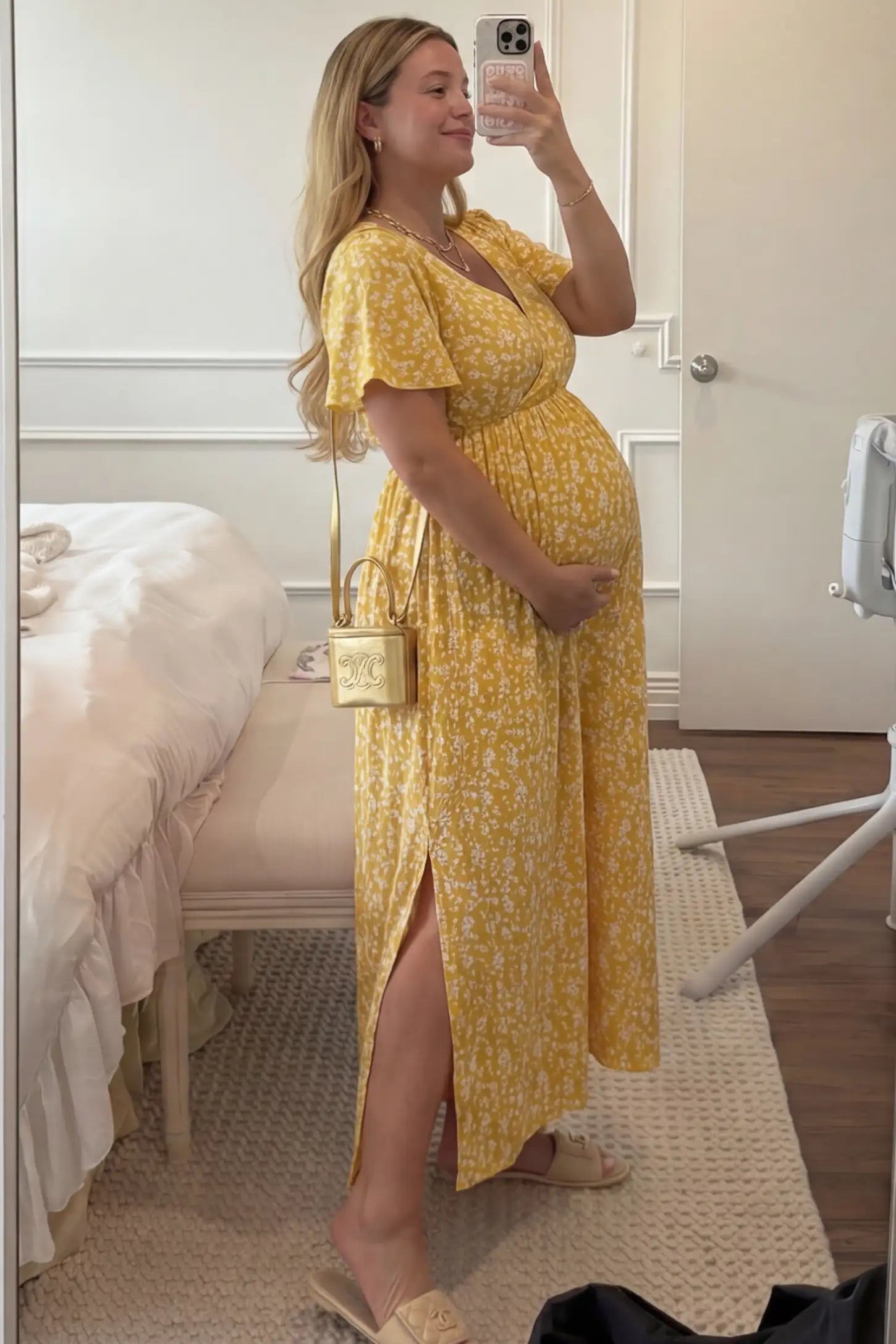Floral V-Neck Side-Slit Maternity Maxi Dress Floral V-Neck Side-Slit Maternity Maxi Dress in yellow featuring short sleeves and a side leg slit, shown on a pregnant woman taking a mirror selfie in a bedroom, side view.