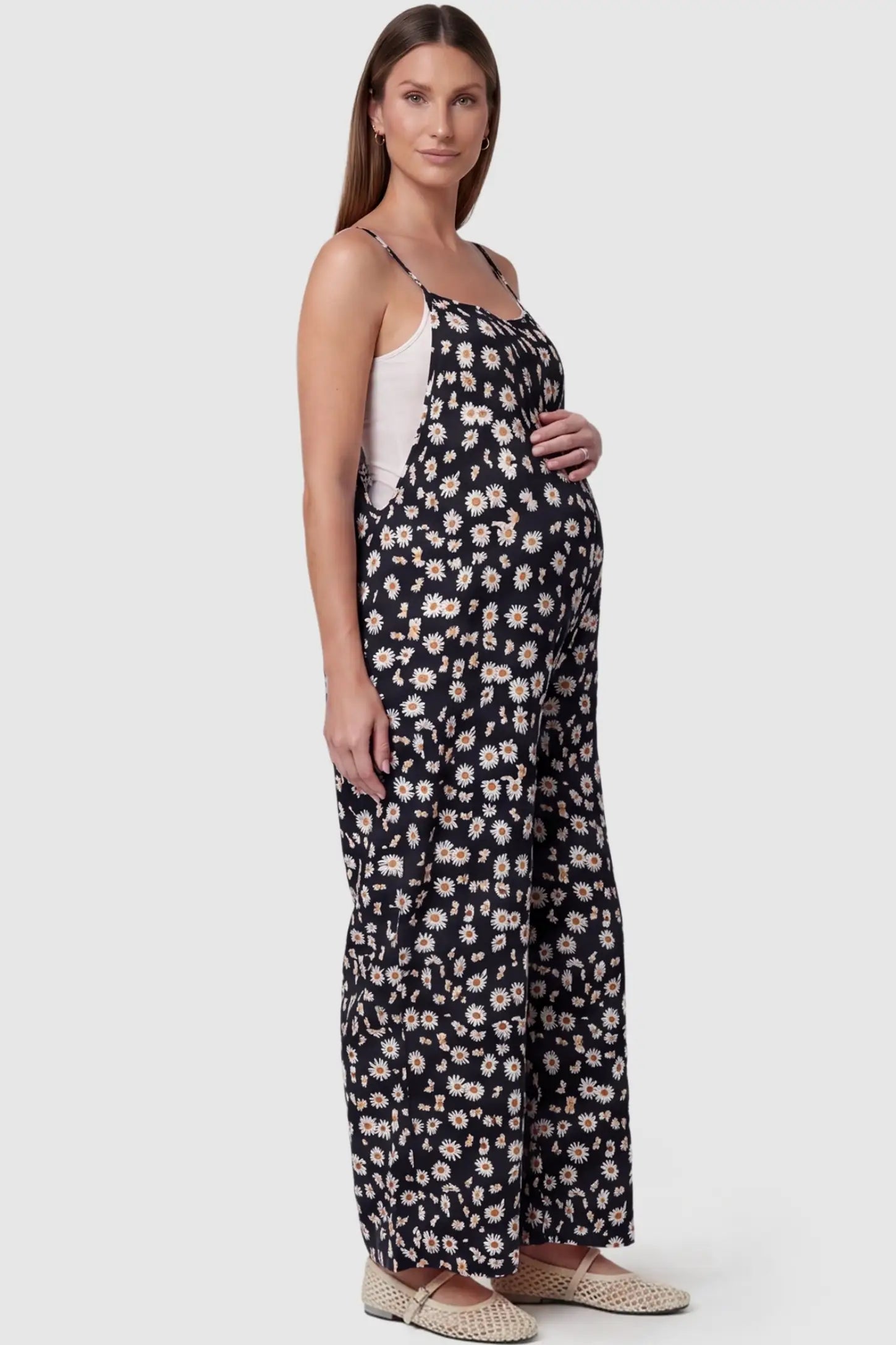Floral Wide-Leg Pocket Maternity Jumpsuit Floral Wide-Leg Pocket Jumpsuit in Black featuring an all-over daisy print on a pregnant model, side view.