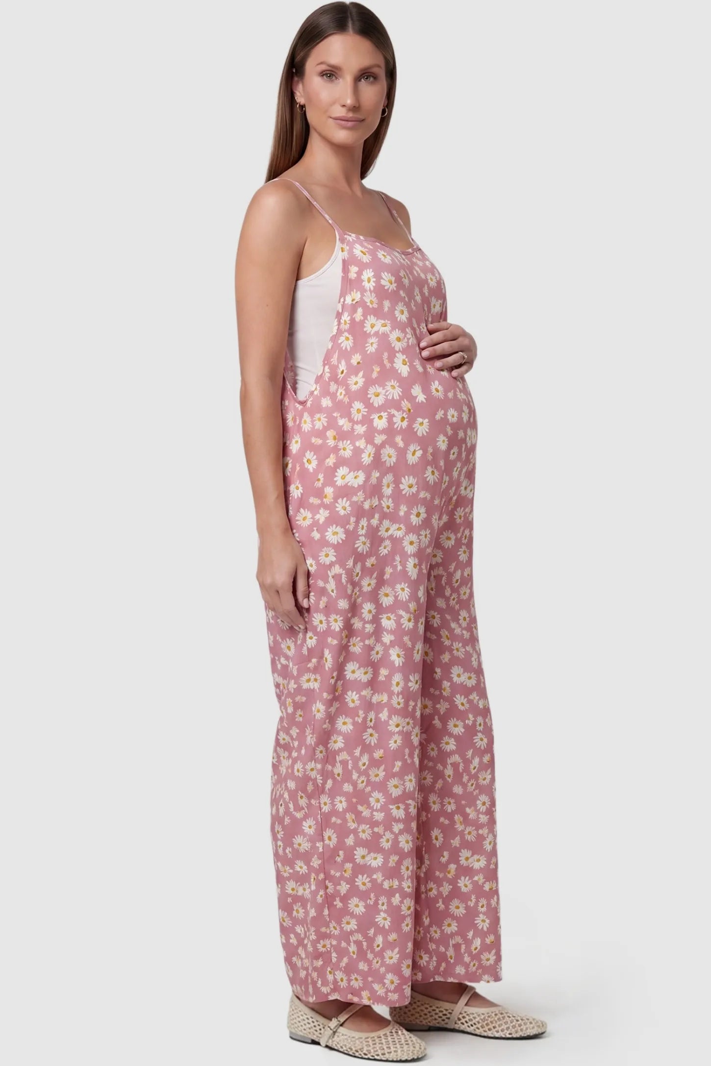 Floral Wide-Leg Pocket Maternity Jumpsuit Floral Wide-Leg Pocket Jumpsuit in Pink featuring an all-over daisy print on a pregnant model, side view.