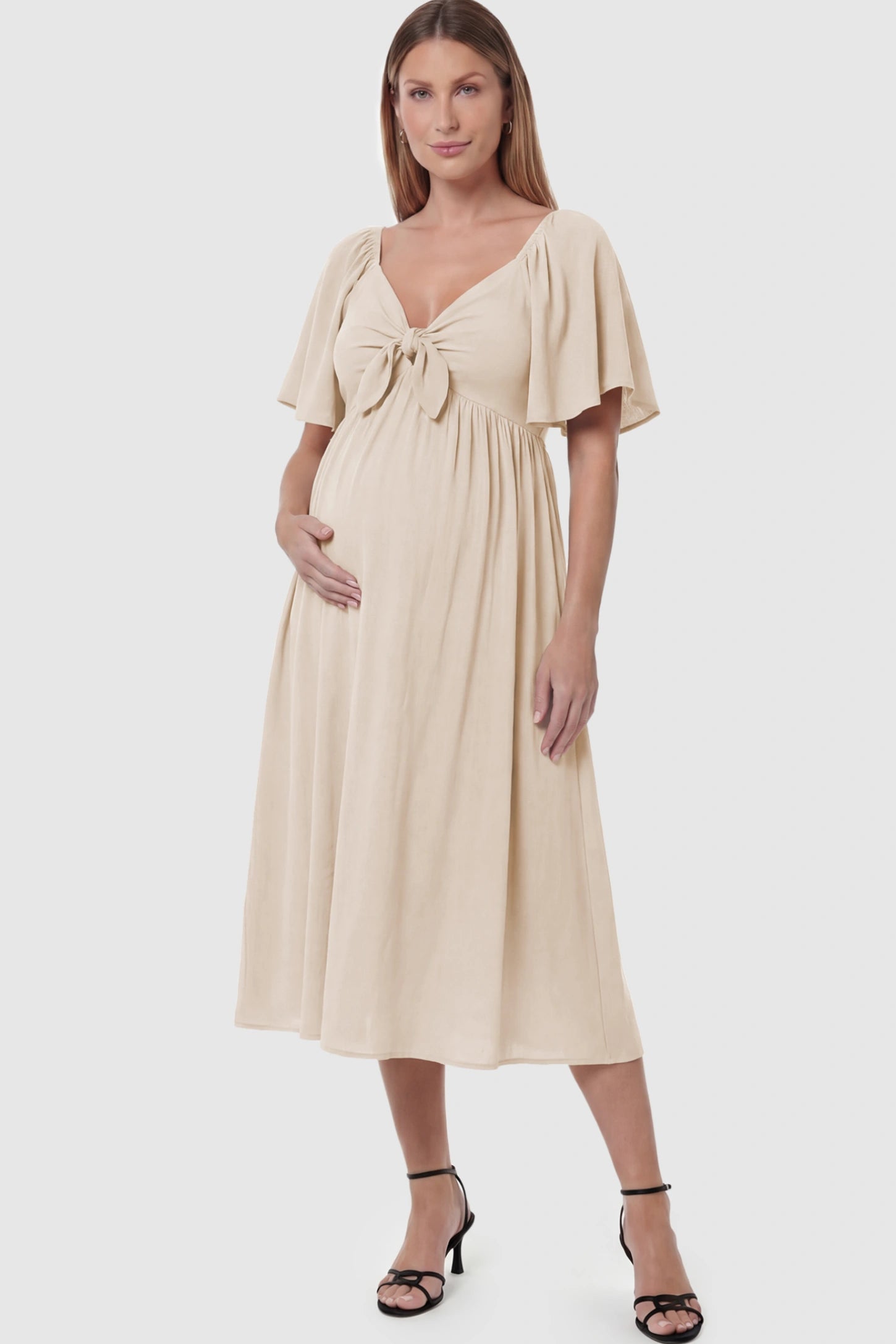Front Tie Flutter Sleeve Maternity Midi Dress Front Tie Flutter Sleeve Maternity Midi Dress in apricot featuring a knotted V-neckline and flowy skirt on a pregnant model posing front.