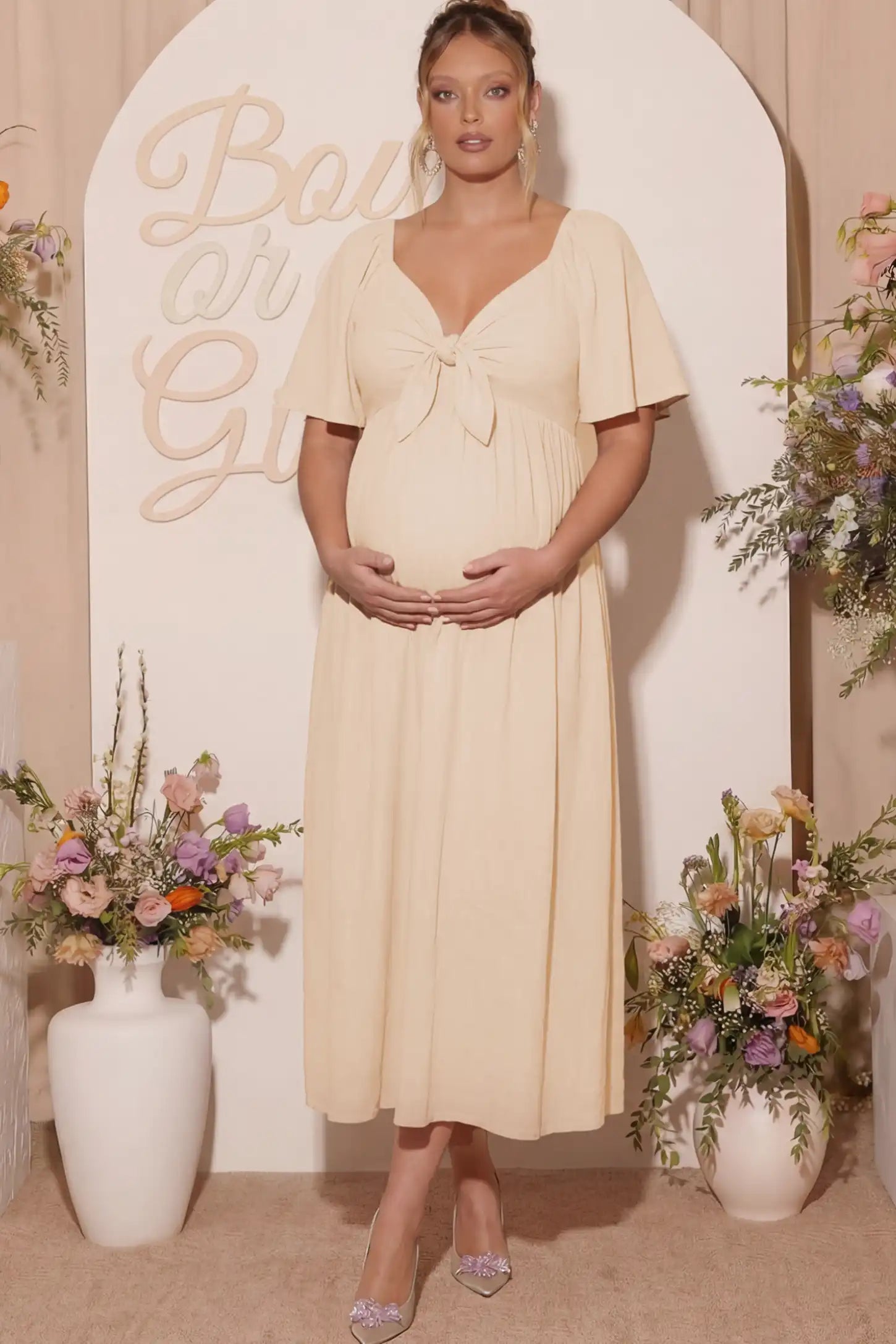 Front Tie Flutter Sleeve Maternity Midi Dress Front Tie Flutter Sleeve Maternity Midi Dress in Apricot featuring a knotted V-neckline and flowy skirt on a pregnant woman.