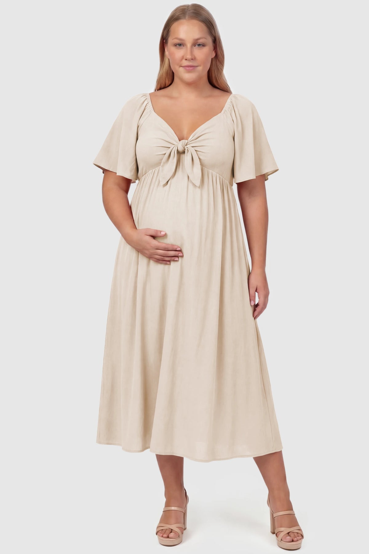 Front Tie Flutter Sleeve Maternity Midi Dress Front Tie Flutter Sleeve Maternity Midi Dress in apricot featuring a knotted V-neckline and flowy skirt on a plus size pregnant model, front view.
