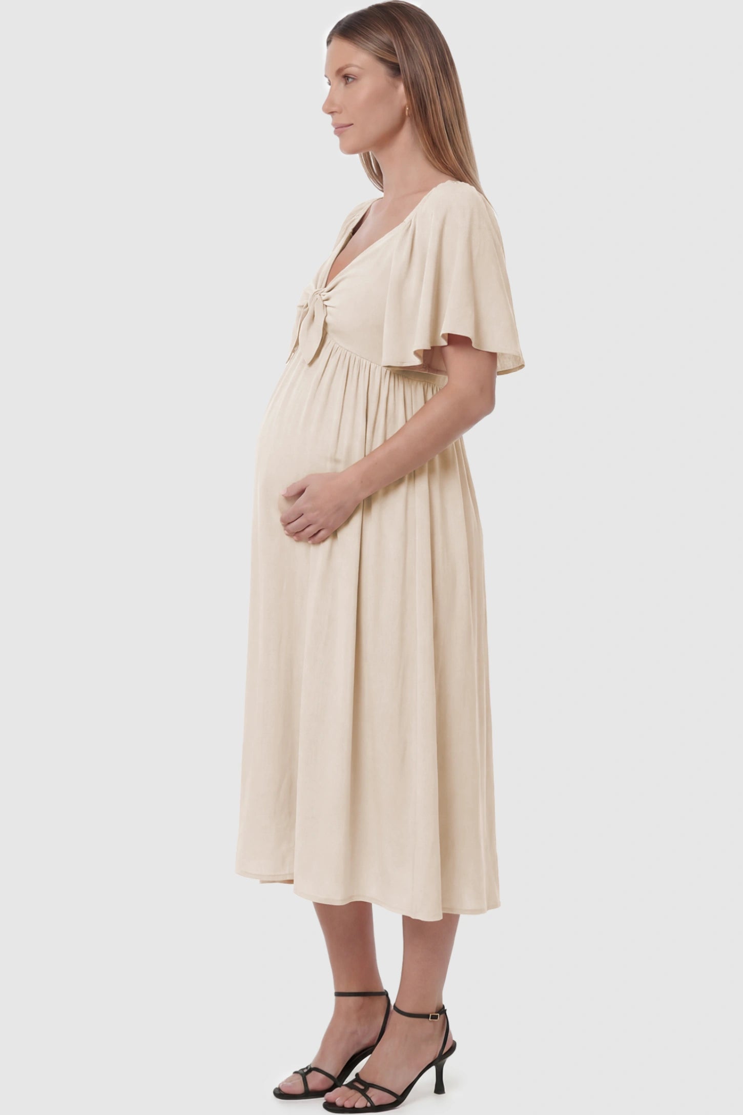 Front Tie Flutter Sleeve Maternity Midi Dress Front Tie Flutter Sleeve Maternity Midi Dress in Apricot featuring a knotted V-neckline and flowy skirt on a pregnant model showing side.
