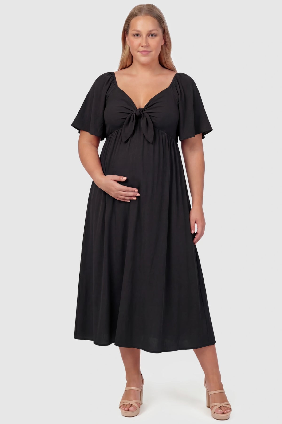 Front Tie Flutter Sleeve Maternity Midi Dress Front Tie Flutter Sleeve Maternity Midi Dress in black featuring a knotted V-neckline and flowy skirt on a plus size pregnant model, front view.