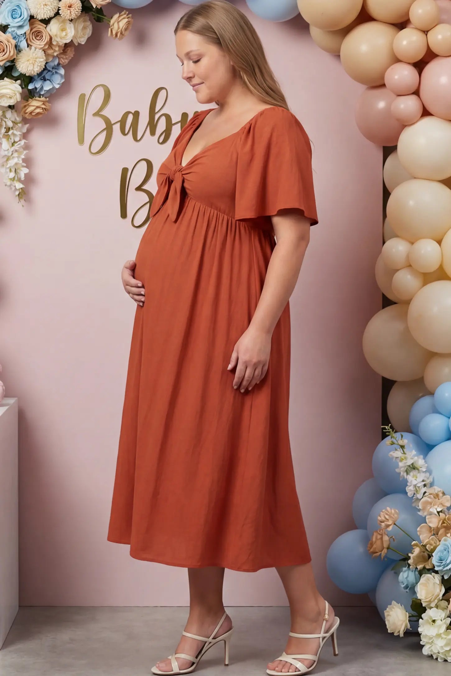 Front Tie Flutter Sleeve Maternity Midi Dress Front Tie Flutter Sleeve Maternity Midi Dress in Brick Red featuring a knotted V-neckline and flowy skirt on a pregnant woman.