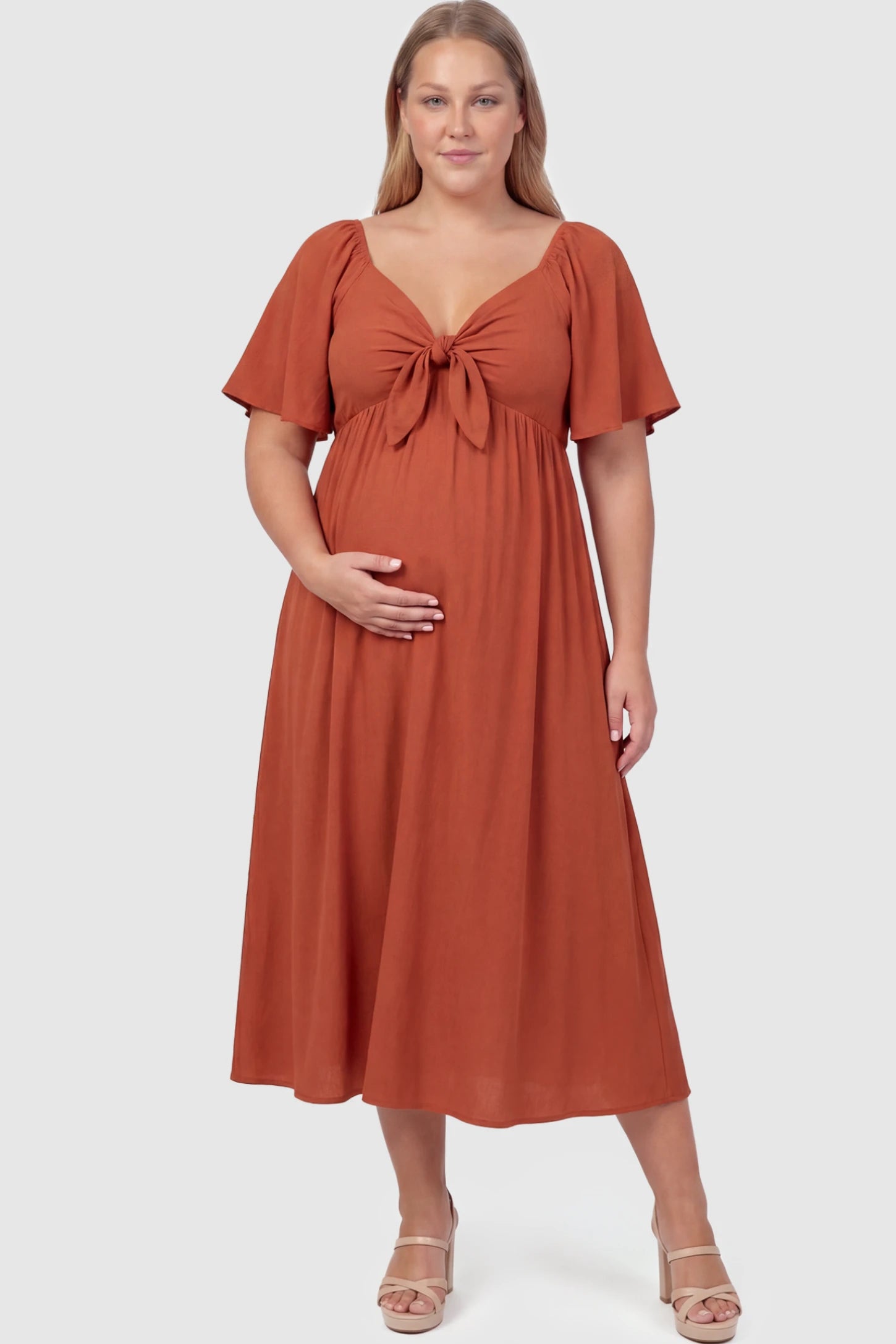 Front Tie Flutter Sleeve Maternity Midi Dress Front Tie Flutter Sleeve Maternity Midi Dress in Brick Red featuring a knotted V-neckline and flowy skirt on a plus size model.