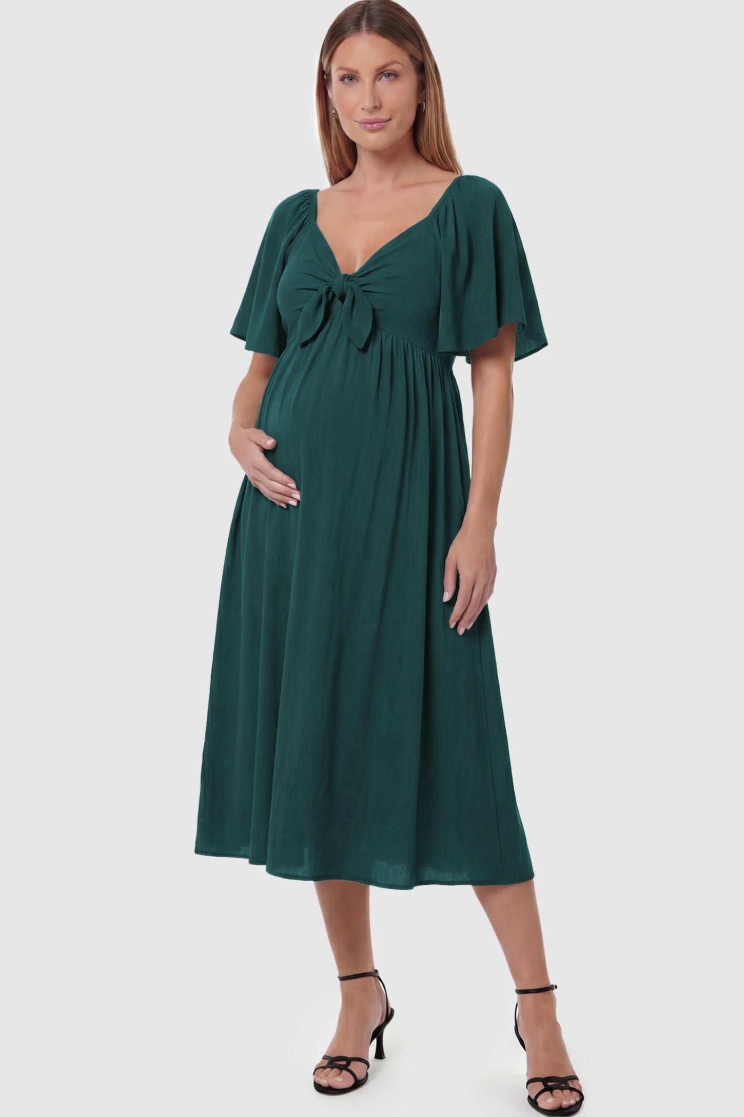 Front Tie Flutter Sleeve Maternity Midi Dress Front Tie Flutter Sleeve Maternity Midi Dress in Emerald Green featuring a knotted V-neckline and flowy skirt on a pregnant model posing front.