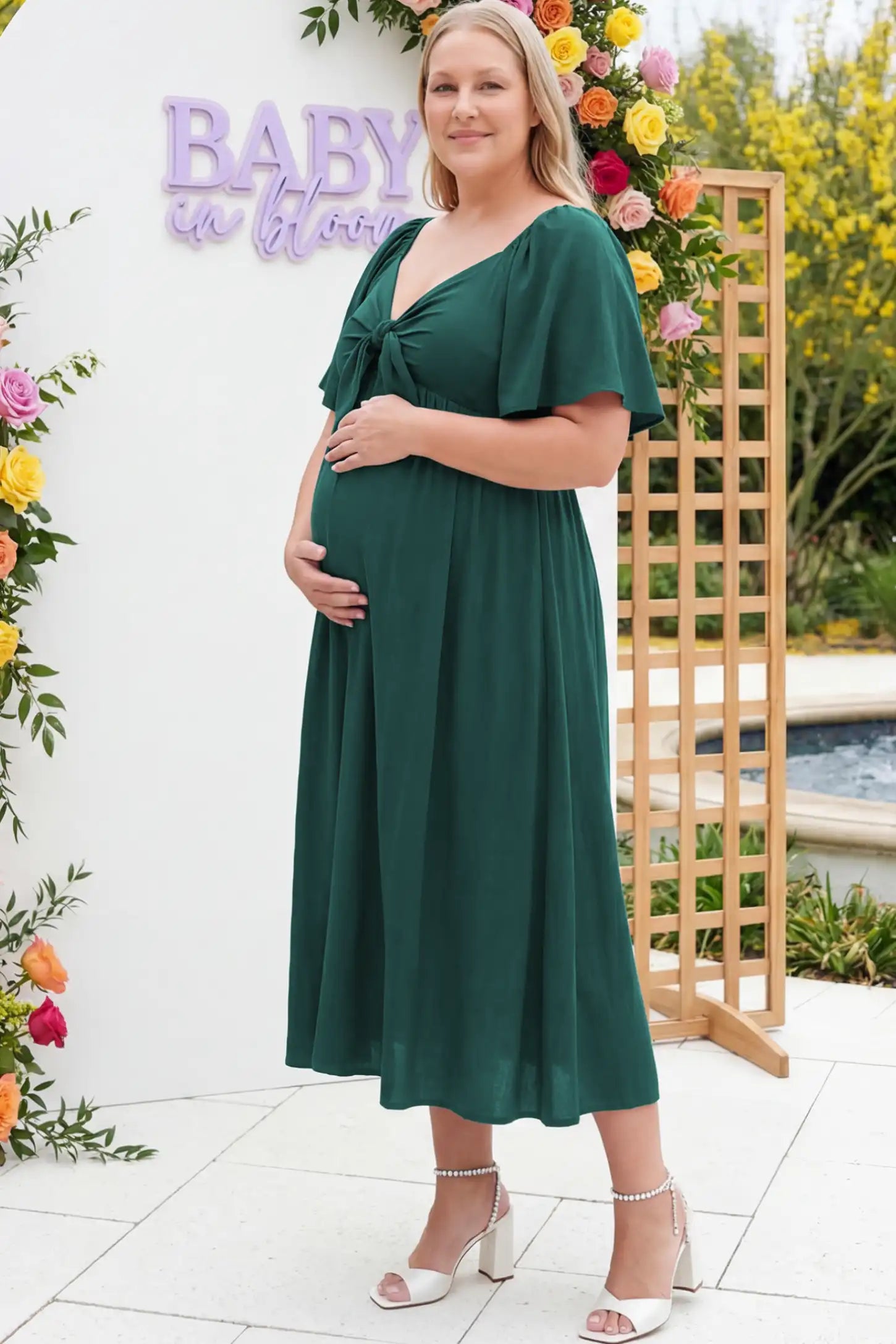 Front Tie Flutter Sleeve Maternity Midi Dress Front Tie Flutter Sleeve Maternity Midi Dress in Emerald Green featuring a knotted V-neckline and flowy skirt on a pregnant woman.