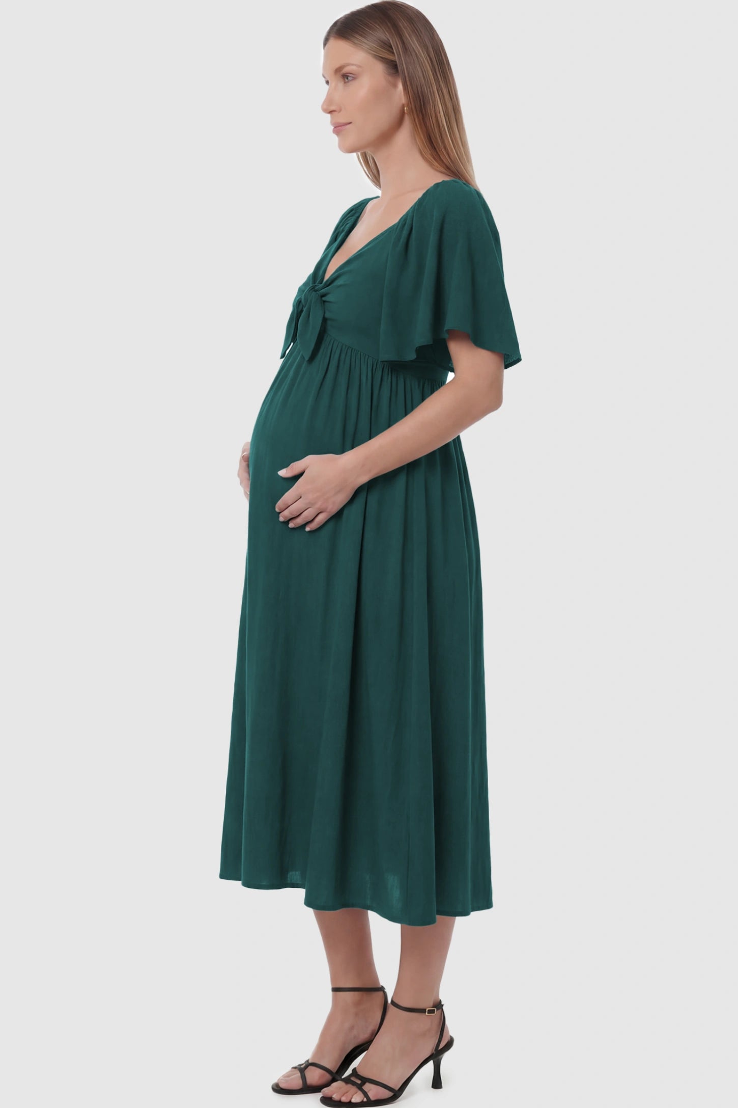 Front Tie Flutter Sleeve Maternity Midi Dress Front Tie Flutter Sleeve Maternity Midi Dress in Emerald Green featuring a knotted V-neckline and flowy skirt on a pregnant model showing side.