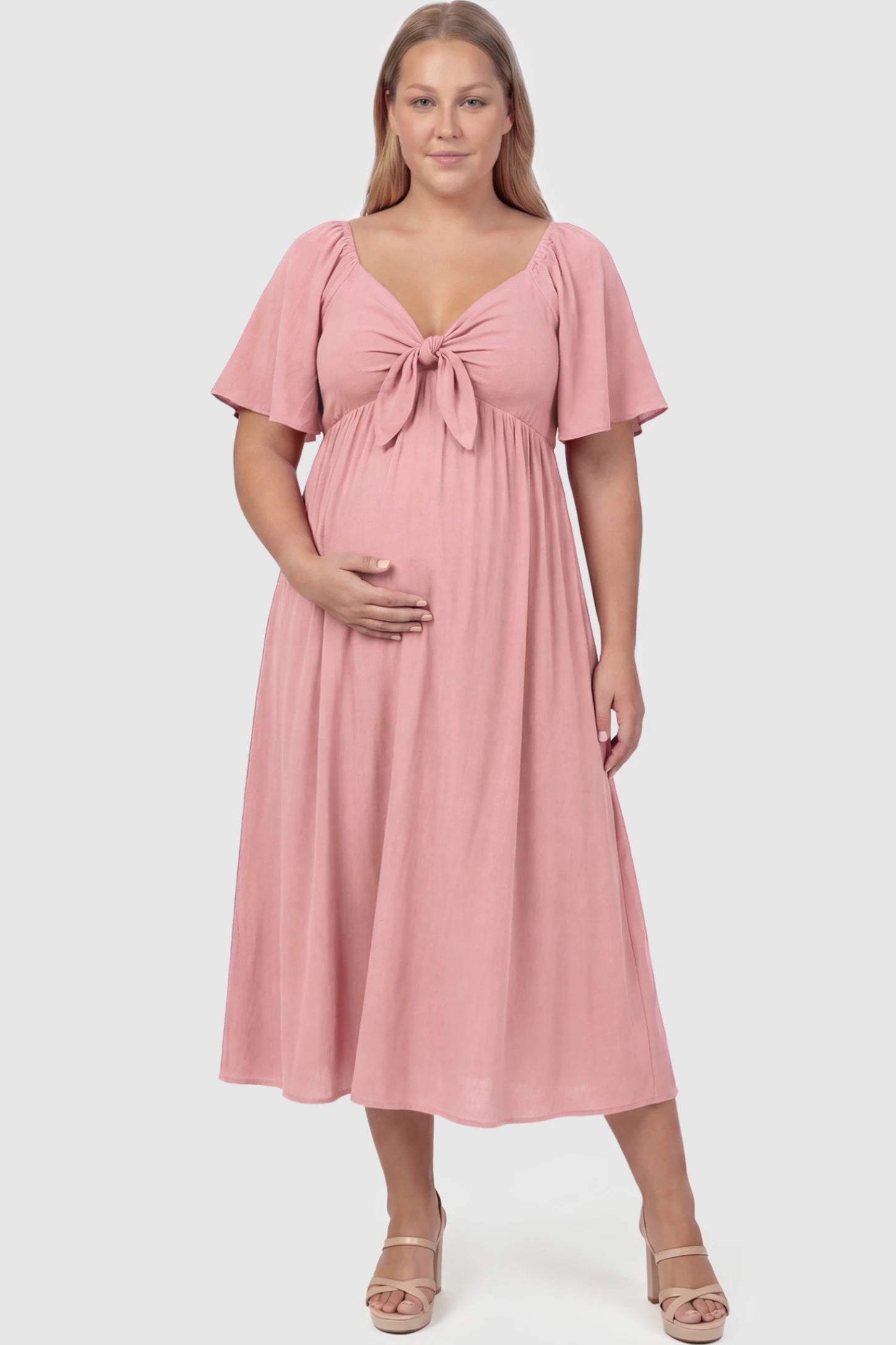 Front Tie Flutter Sleeve Maternity Midi Dress Front Tie Flutter Sleeve Maternity Midi Dress in pink featuring a knotted V-neckline and flowy skirt on a plus size model showing front.