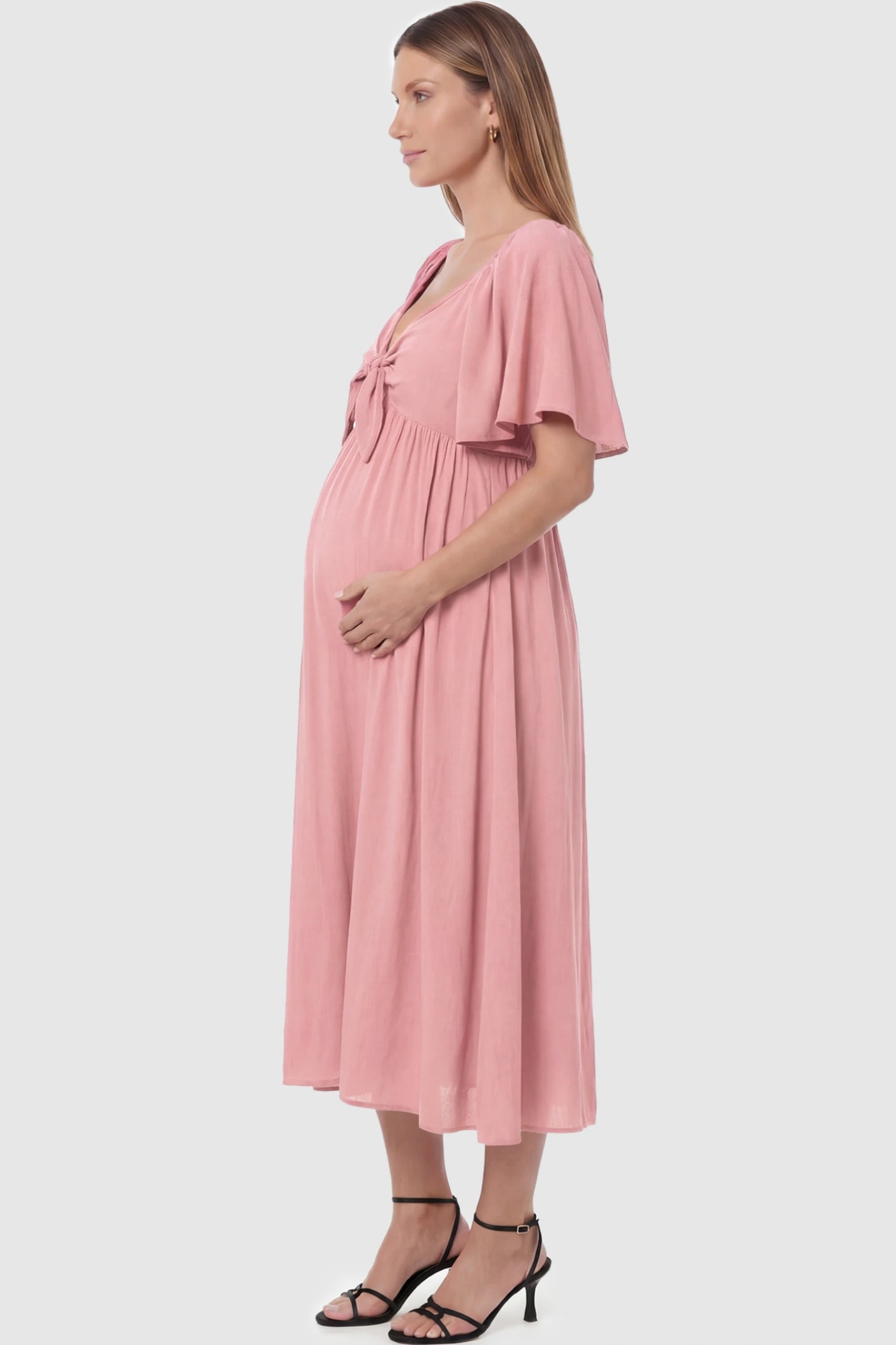 Front Tie Flutter Sleeve Maternity Midi Dress Front Tie Flutter Sleeve Maternity Midi Dress in pink featuring a knotted V-neckline and flowy skirt on a pregnant model showing side.