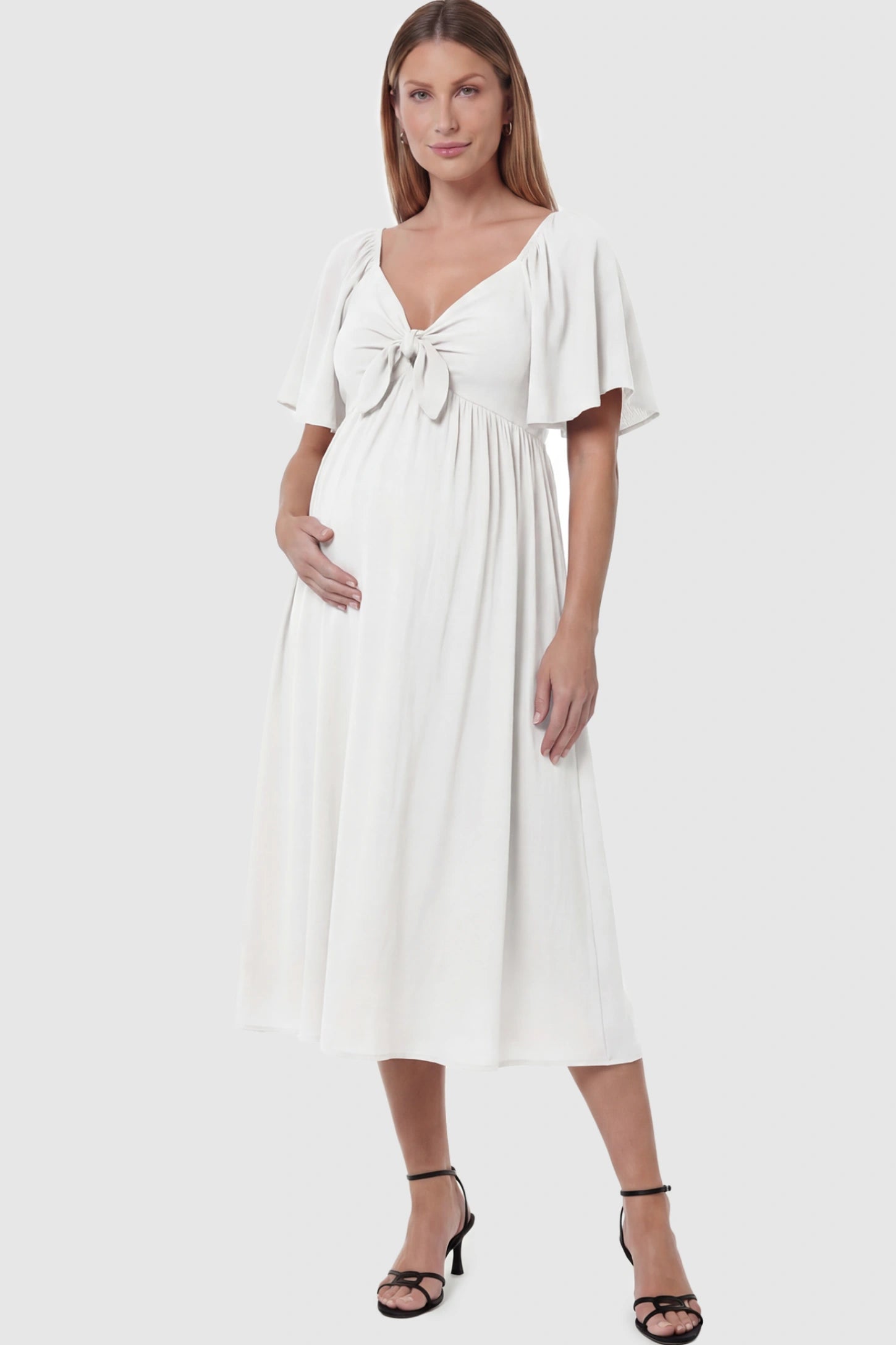 Front Tie Flutter Sleeve Maternity Midi Dress Front Tie Flutter Sleeve Maternity Midi Dress in white featuring a knotted V-neckline and flowy skirt on a pregnant model posing front.