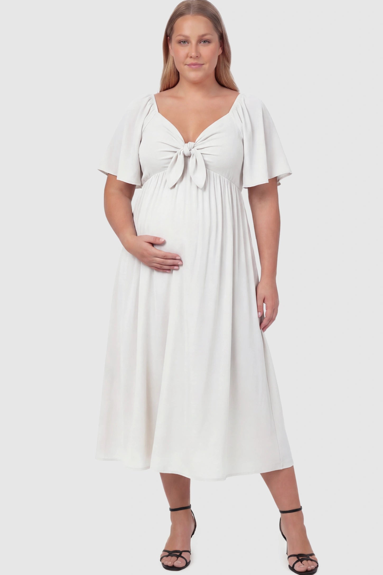 Front Tie Flutter Sleeve Maternity Midi Dress Front Tie Flutter Sleeve Maternity Midi Dress in white featuring a knotted V-neckline and flowy skirt on a plus size model.