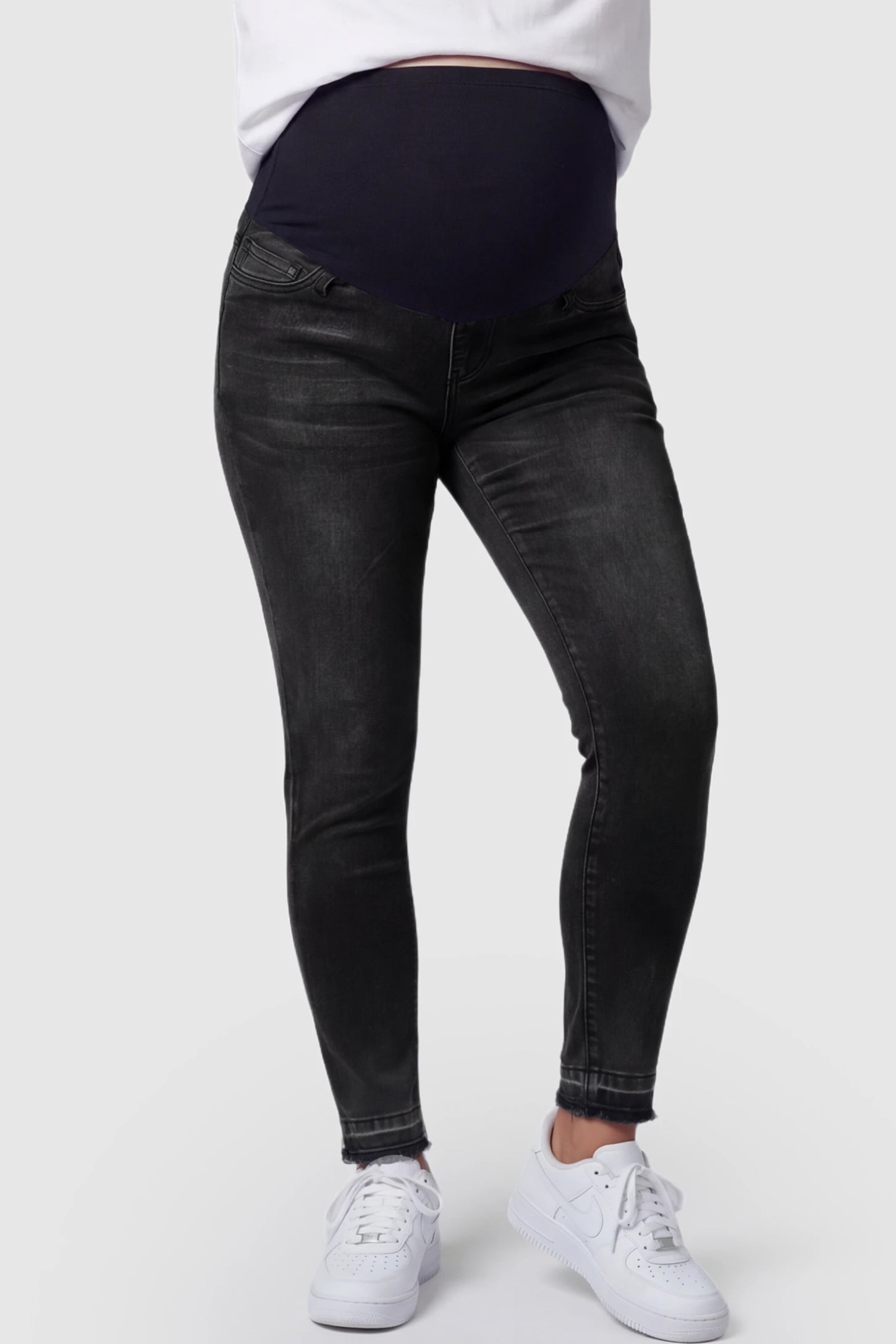 Full Panel Released Hem Maternity Skinny Jeans Full Panel Released Hem Maternity Skinny Jeans in Black featuring a released hem and over-the-belly panel on a pregnant model showing front.