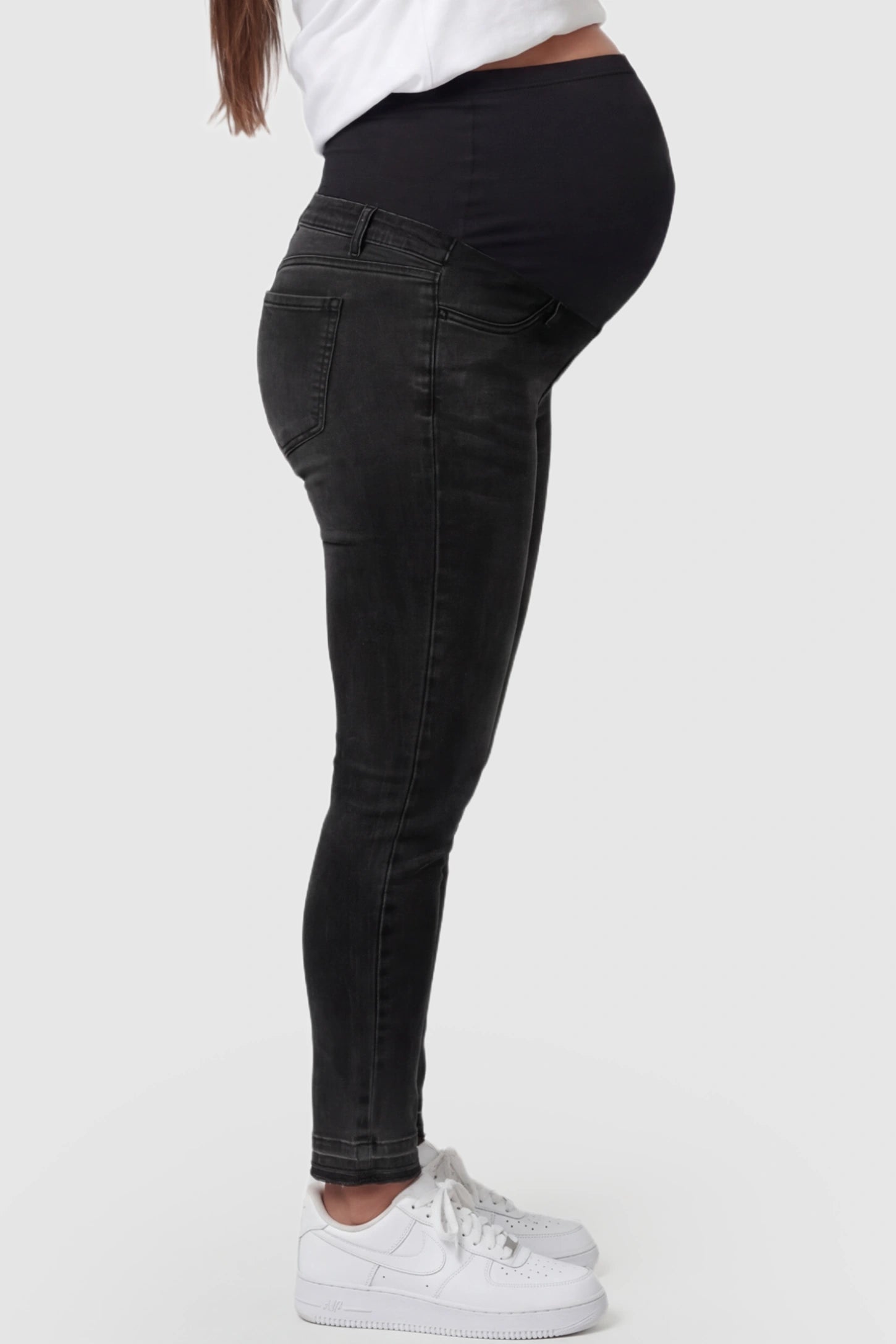 Full Panel Released Hem Maternity Skinny Jeans Full Panel Released Hem Maternity Skinny Jeans in Black featuring a released hem and over-the-belly panel on a pregnant model showing side.