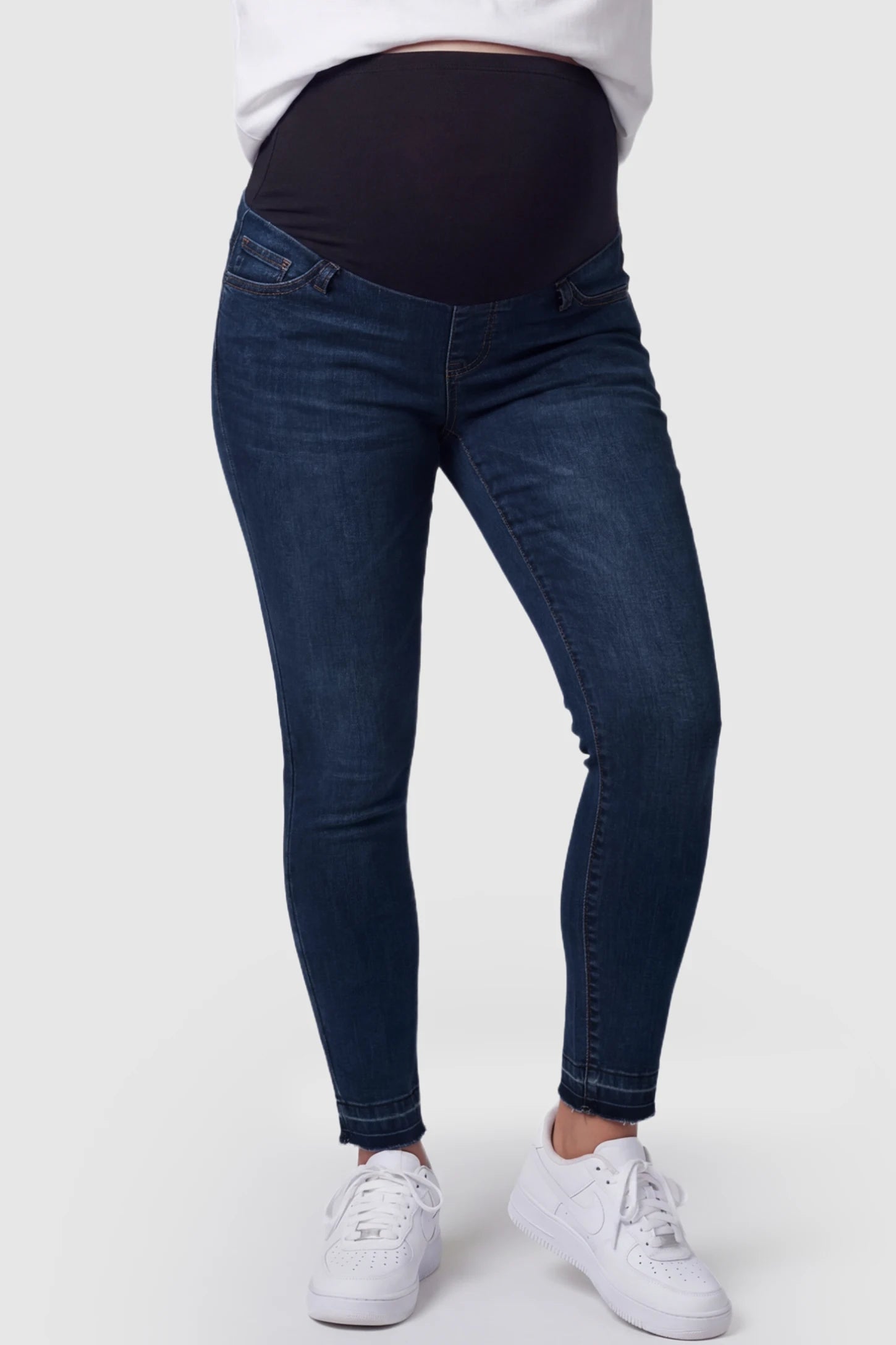 Full Panel Released Hem Maternity Skinny Jeans Full Panel Released Hem Maternity Skinny Jeans in Dark Blue featuring a released hem and over-the-belly panel on a pregnant model showing front.