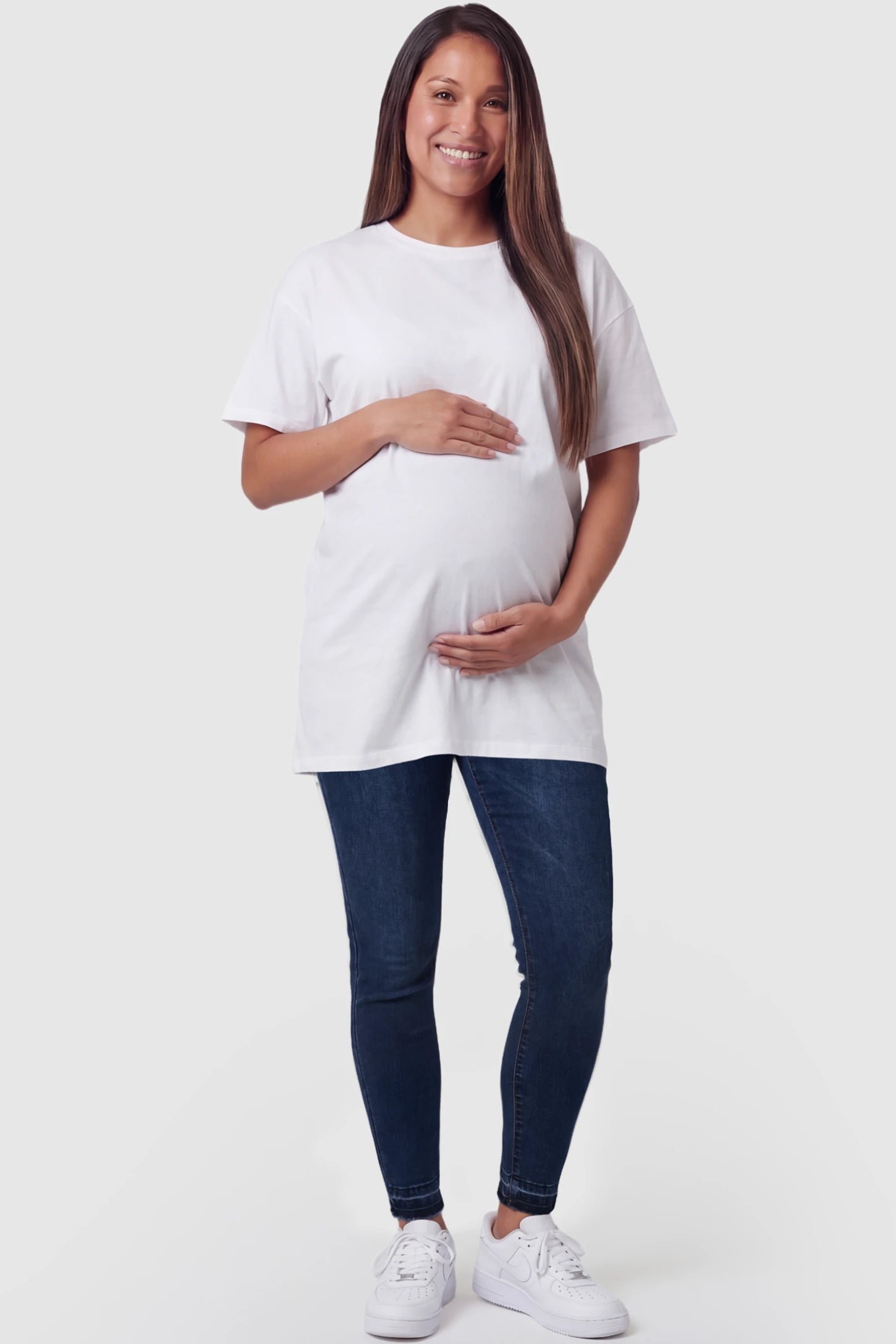 Full Panel Released Hem Maternity Skinny Jeans Full Panel Released Hem Maternity Skinny Jeans in Dark Blue featuring a released hem and over-the-belly panel on a pregnant model facing front.