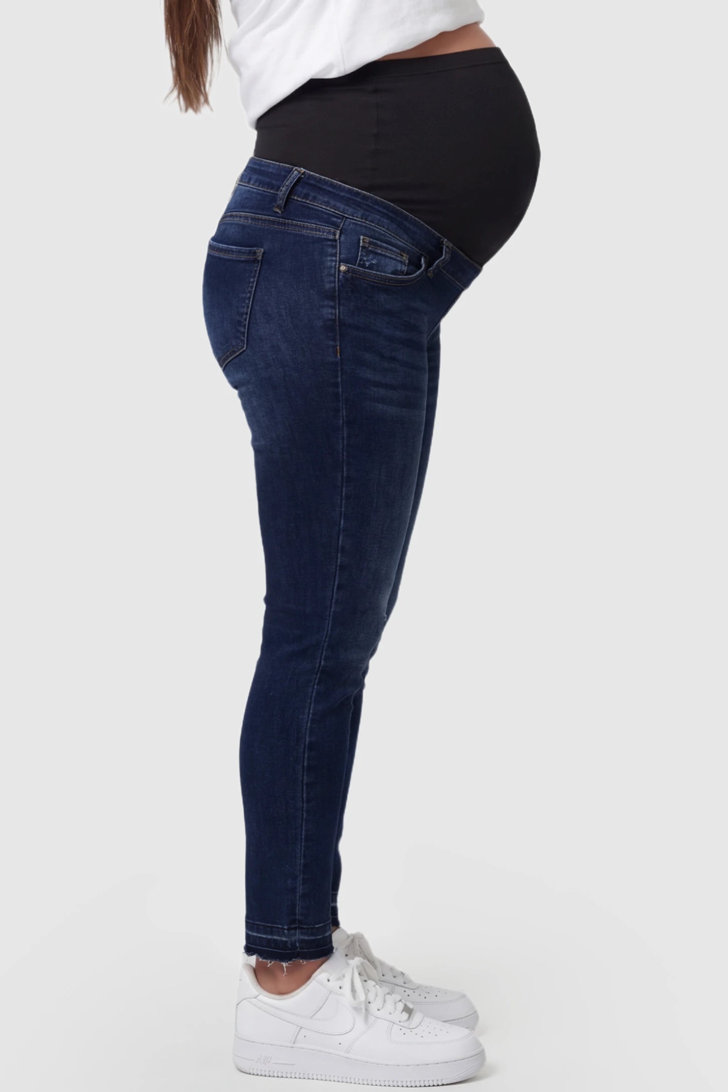 Full Panel Released Hem Maternity Skinny Jeans Full Panel Released Hem Maternity Skinny Jeans in Dark Blue featuring a released hem and over-the-belly panel on a pregnant model showing side.