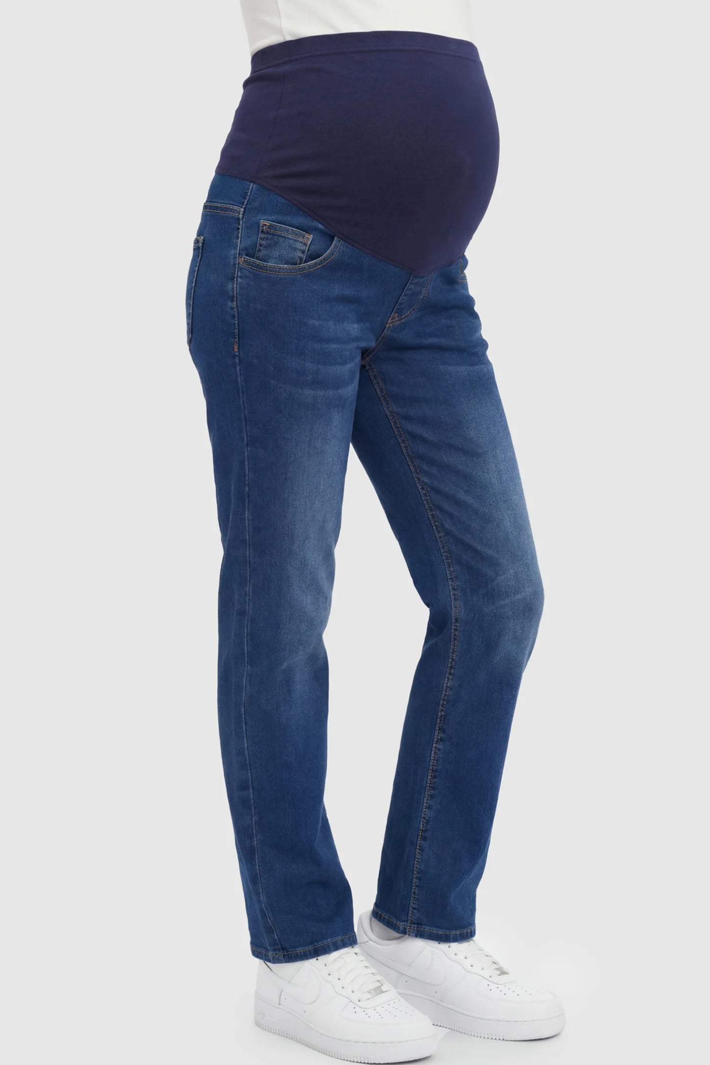 Full Panel Stretch Straight Leg Maternity Jeans Full Panel Stretch Straight Leg Maternity Jeans in Blue featuring a seamless navy waistband on a pregnant model showing side.