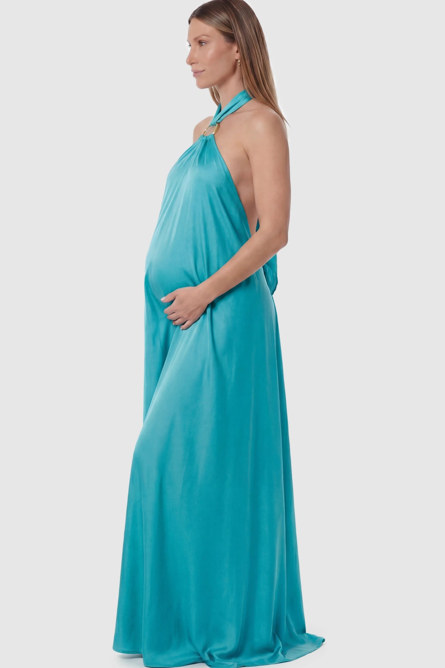 Solid Halter Neck Maternity Maxi Dress Solid Halter Neck Maternity Maxi Dress in Blue featuring a flowing skirt and backless design on a pregnant model showing side.