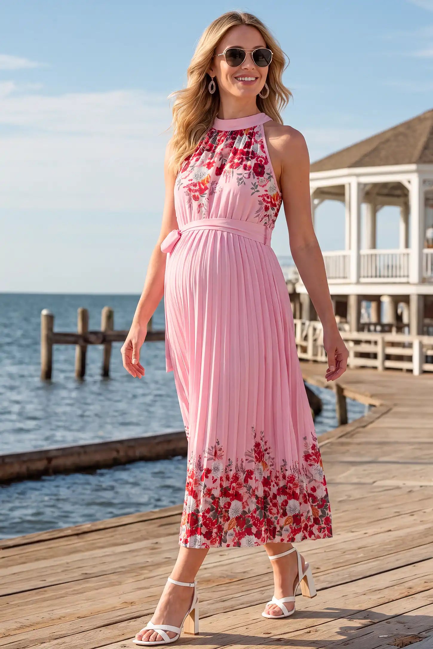 Halter Neck Pleated Maternity Midi Dress Halter Neck Pleated Maternity Midi Dress in Rose Pink Floral showing an elegant pleated A-line skirt on a pregnant model, lifestyle side view.