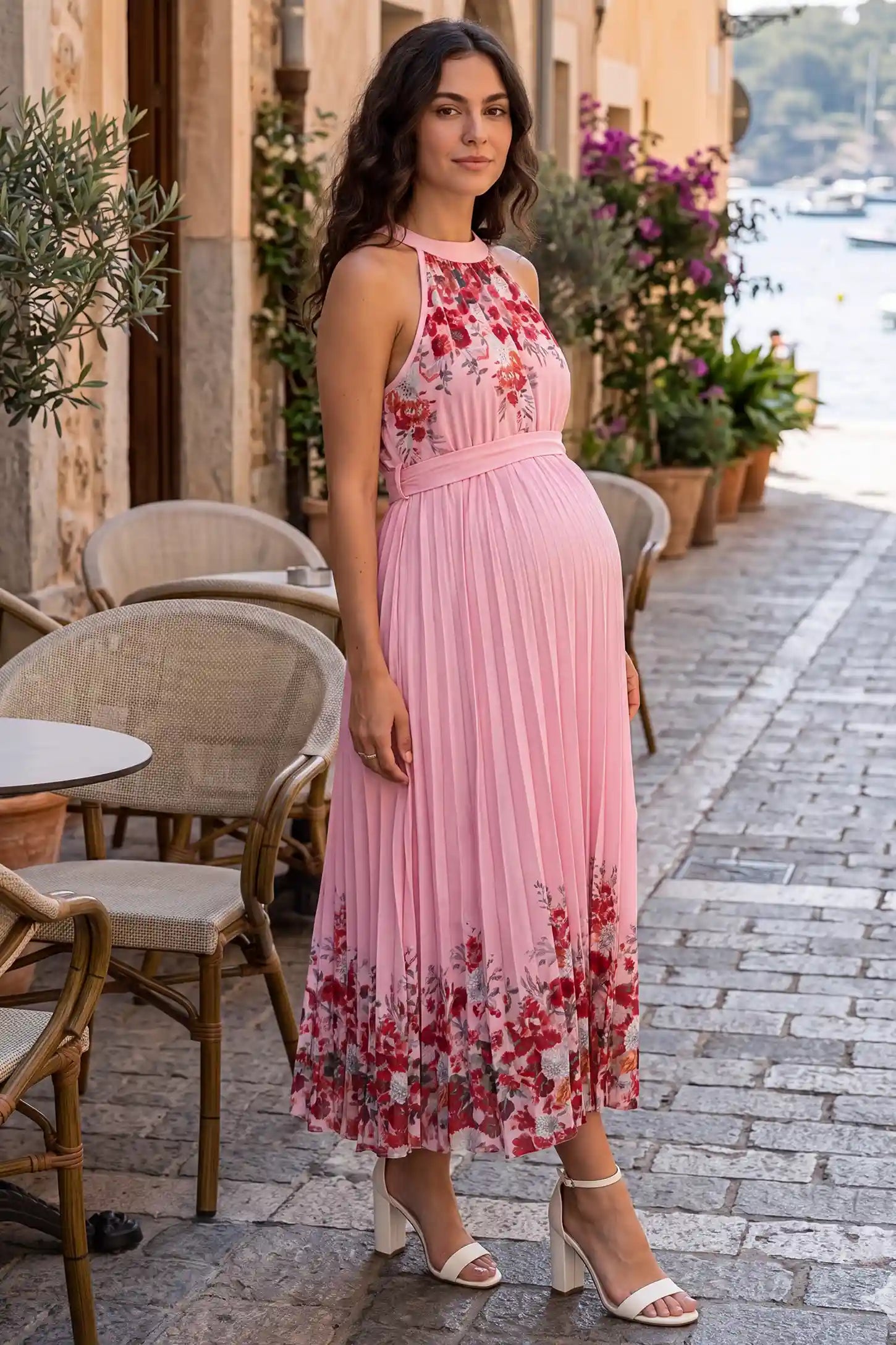 Halter Neck Pleated Maternity Midi Dress Halter Neck Pleated Maternity Midi Dress in Rose Pink Floral showing an elegant pleated A-line skirt on a pregnant model, lifestyle side view.