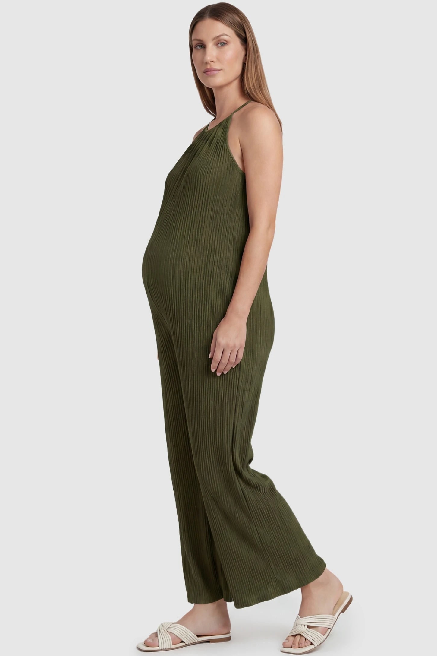 Halter Neck Wide Leg Pocketed Maternity Jumpsuit Halter Neck Wide Leg Pocketed Maternity Jumpsuit in Army Green featuring a ribbed halter neck design on a pregnant model, side view.