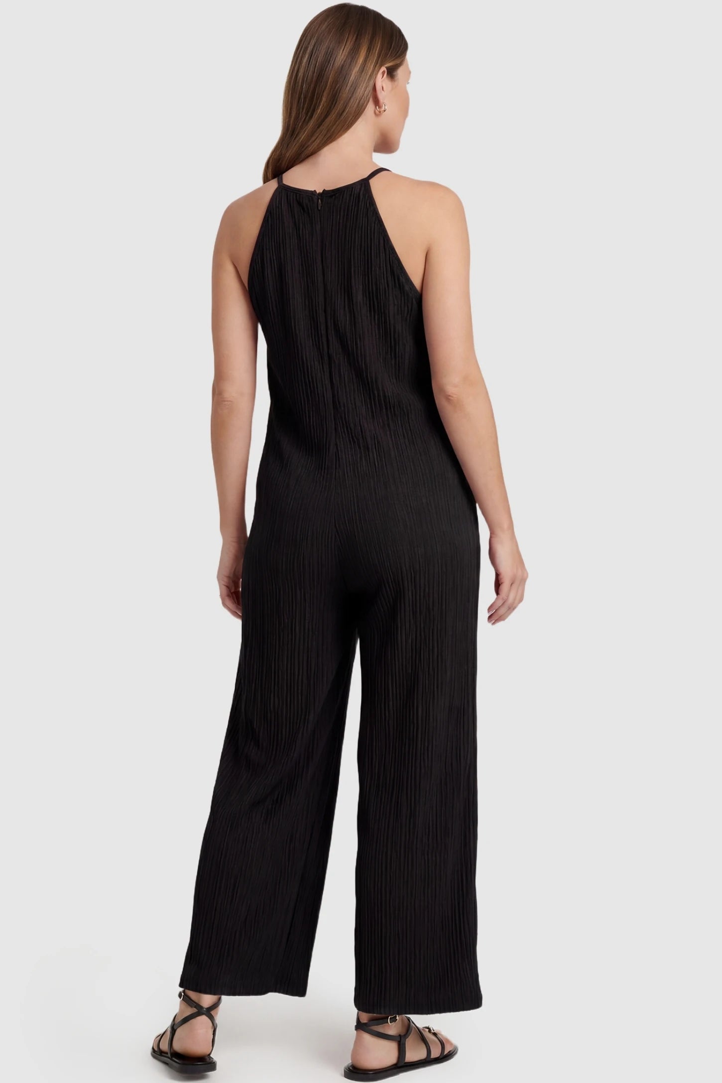 Halter Neck Wide Leg Pocketed Maternity Jumpsuit Halter Neck Wide Leg Pocketed Maternity Jumpsuit in Black featuring a halter neck and allover ribbing on a pregnant model, back view.