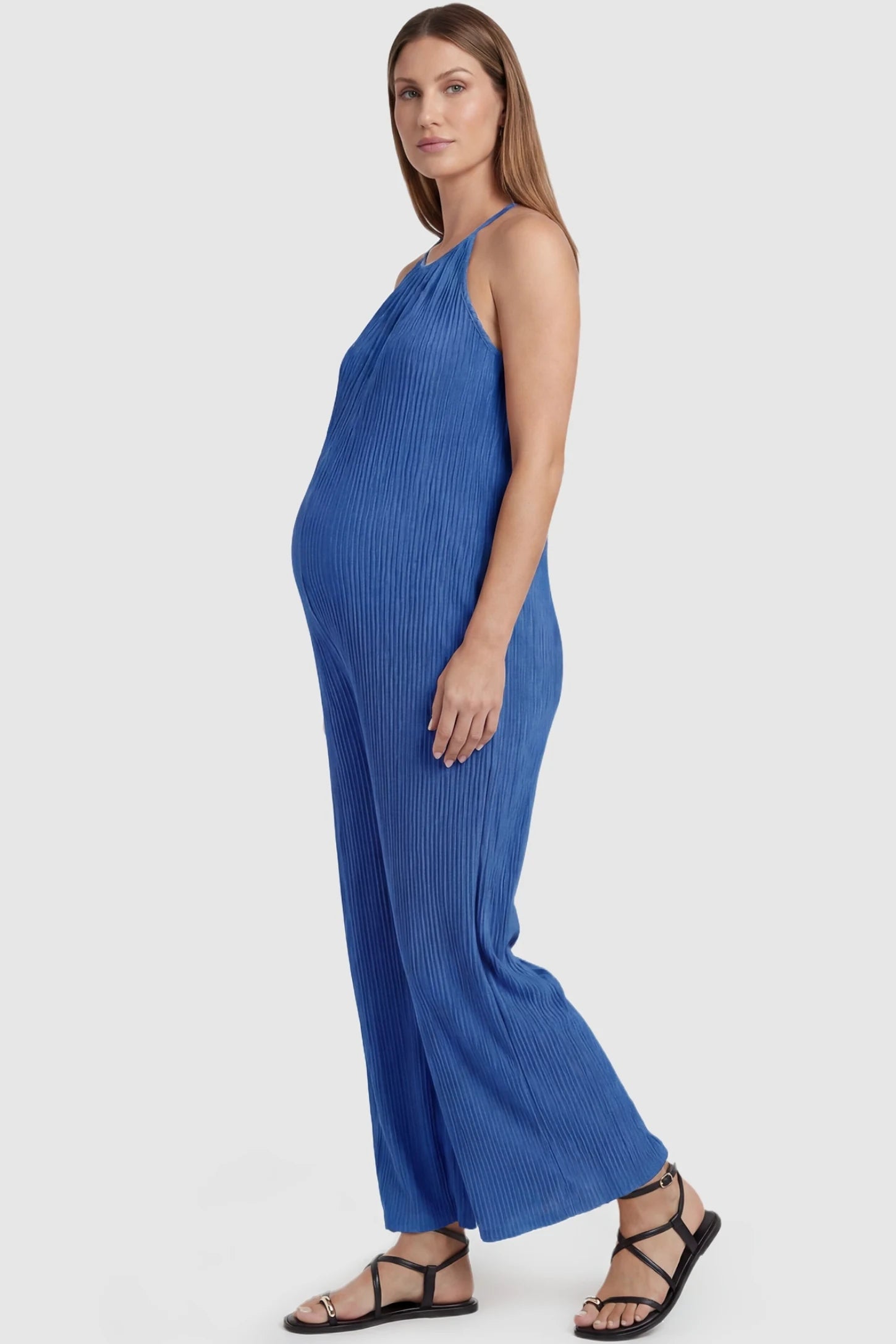 Halter Neck Wide Leg Pocketed Maternity Jumpsuit Halter Neck Wide Leg Pocketed Maternity Jumpsuit in Blue featuring a ribbed halter neck design on a pregnant model, side view.