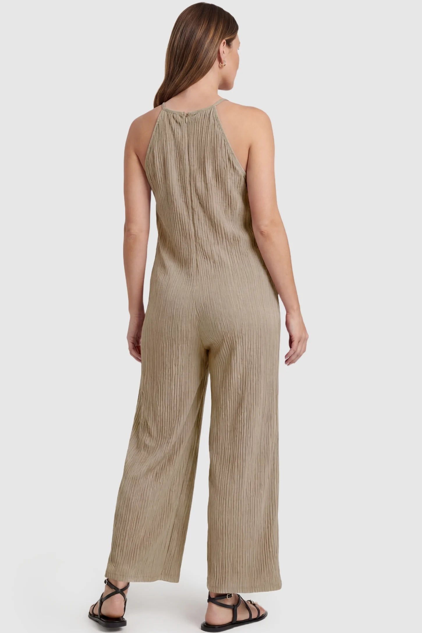 Halter Neck Wide Leg Pocketed Maternity Jumpsuit Halter Neck Wide Leg Pocketed Maternity Jumpsuit in Khaki featuring a halter neck and allover ribbing on a pregnant model, back view.