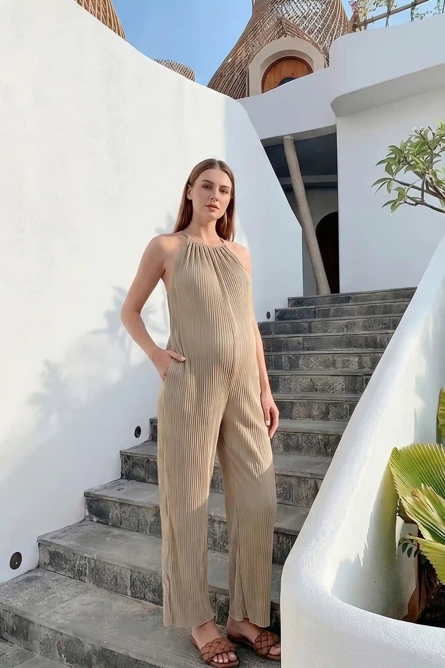 Halter Neck Wide Leg Pocketed Maternity Jumpsuit Halter Neck Wide Leg Pocketed Maternity Jumpsuit in Khaki featuring a ribbed halter neckline on a pregnant model, editorial lifestyle view.