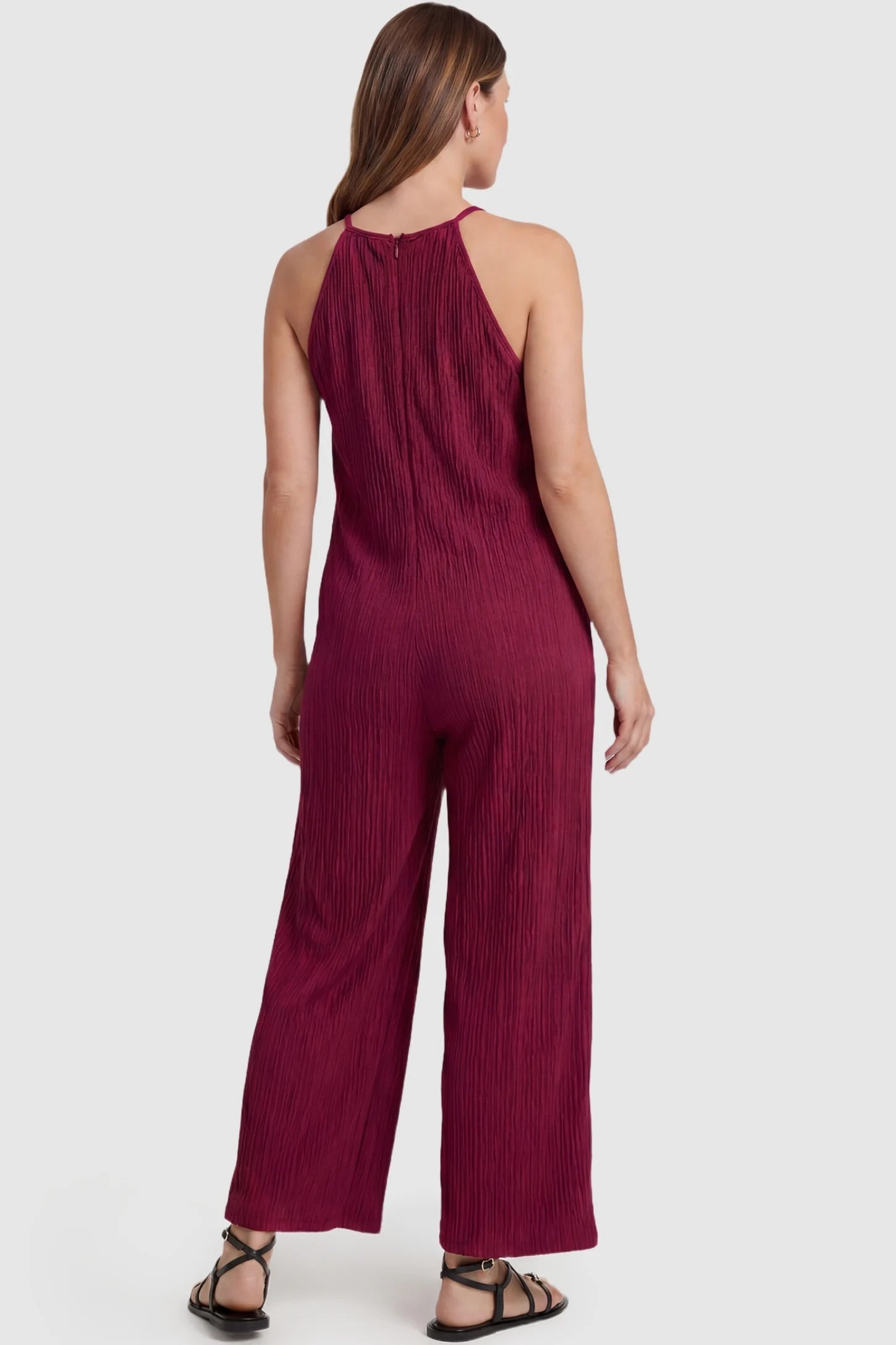 Halter Neck Wide Leg Pocketed Maternity Jumpsuit Halter Neck Wide Leg Pocketed Maternity Jumpsuit in Wine Red featuring a halter neck and allover ribbing on a pregnant model, back view.