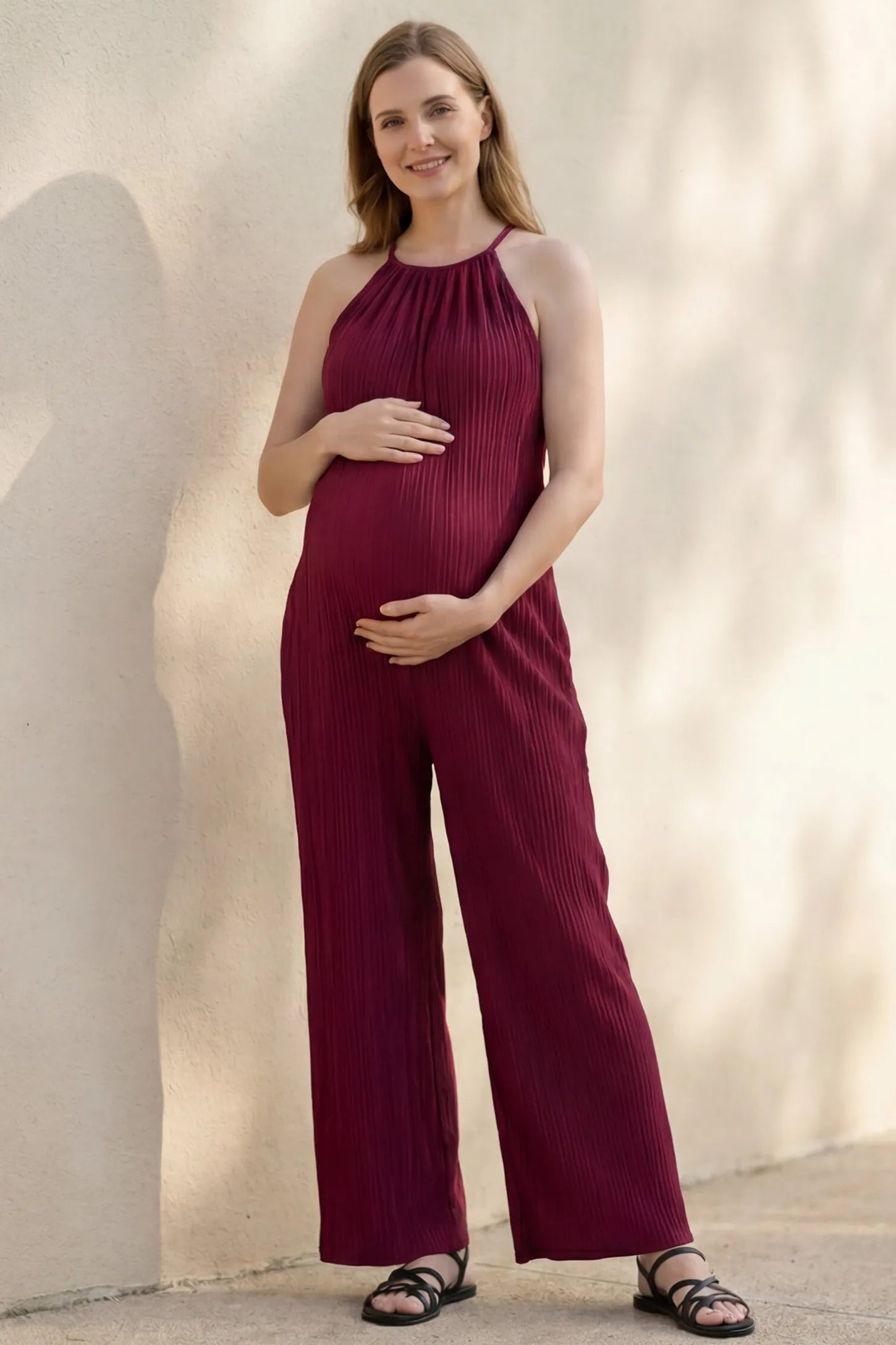 Halter Neck Wide Leg Pocketed Maternity Jumpsuit Halter Neck Wide Leg Pocketed Maternity Jumpsuit in Wine Red featuring a ribbed halter neckline on a pregnant model, editorial lifestyle view.